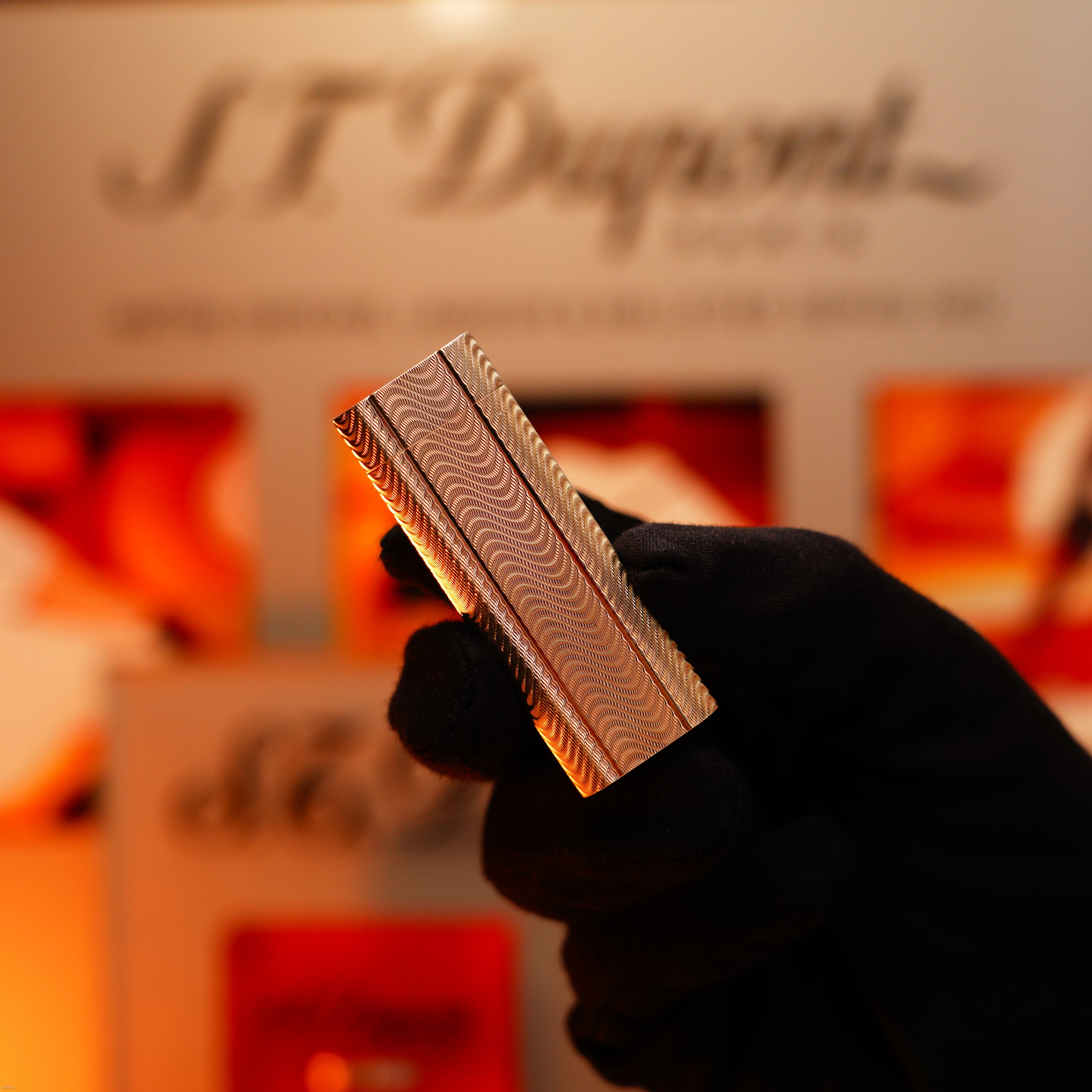 A gloved hand presents the Lucy Lighter Vintage 1970 Early Cartier Production Heavy Silver Rare Guilloché Pattern Lighter; a blurred sign and warm tones highlight its timeless sophistication.