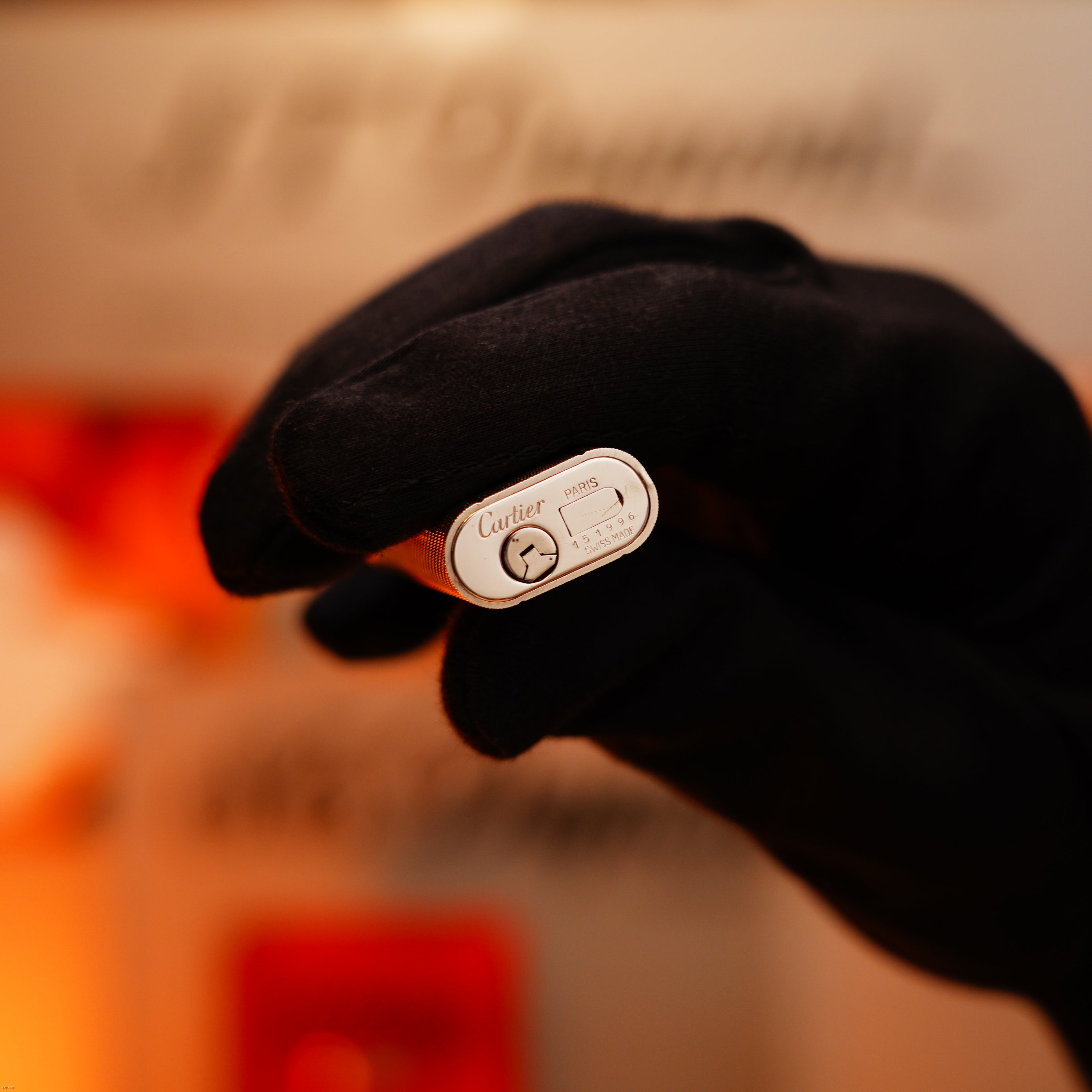 A gloved hand holds a Vintage 1970 Lucy Lighter, featuring rare Cartier early production with heavy silver guilloché pattern, engraved branding, and a visible gas adjustment wheel on the bottom.