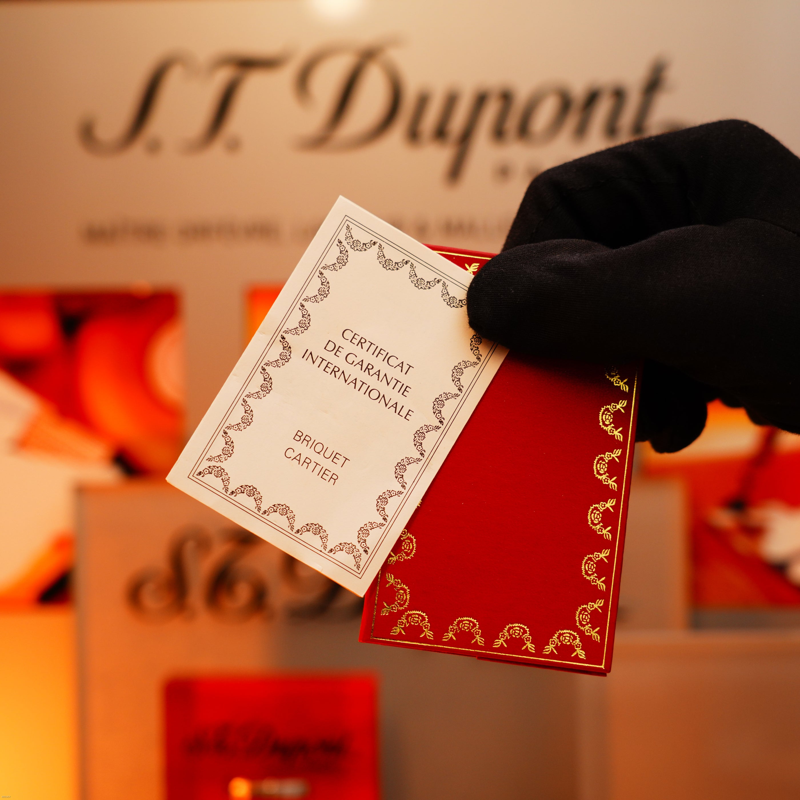 A gloved hand holds a red card and a "Certificat De Garantie Internationale," showcasing the quality of a Vintage 1970 Early Cartier Production Heavy Silver Rare Guilloché Pattern Lighter by Lucy Lighter.