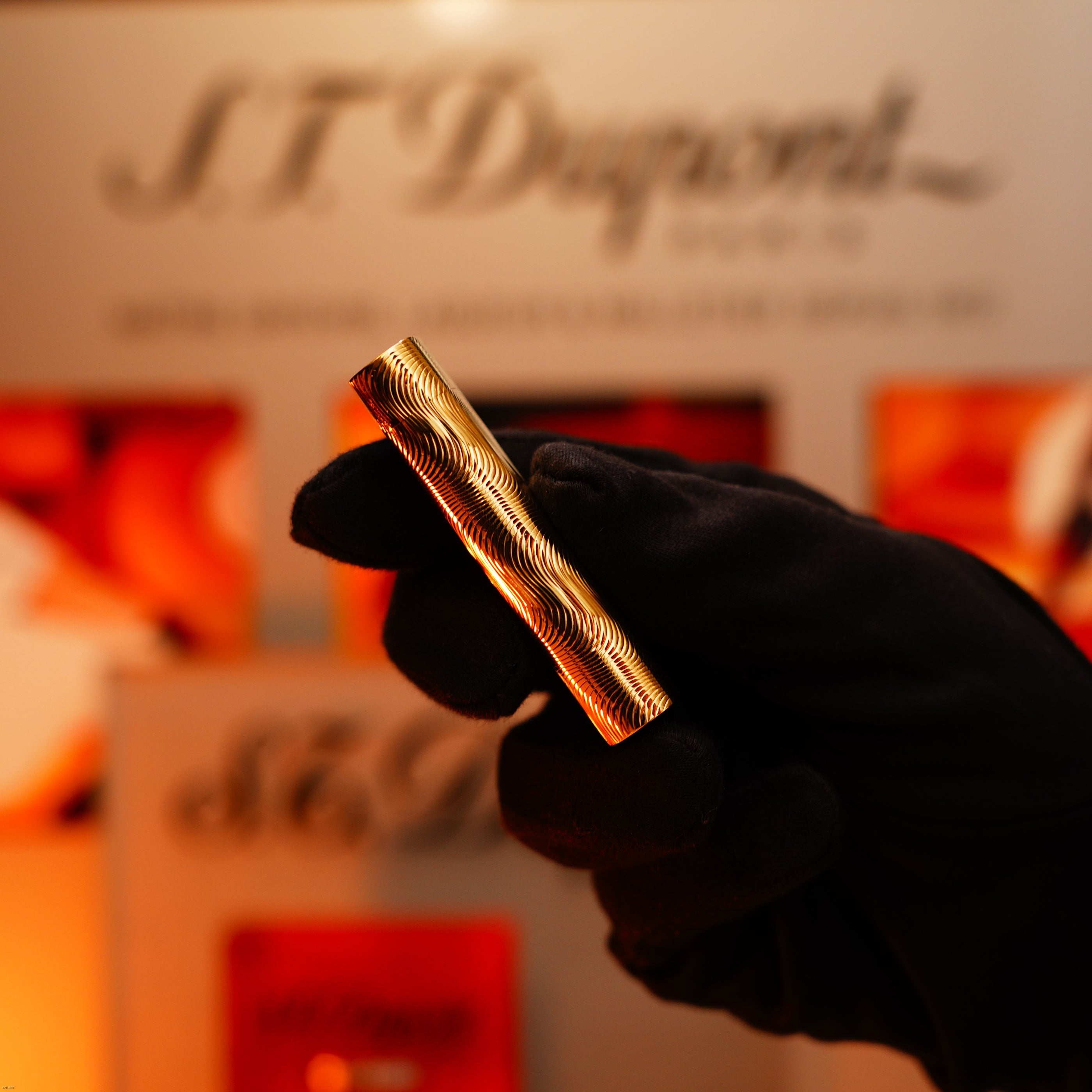 A gloved hand holds a Vintage 1970 Cartier Lucy Lighter—an extremely rare, heavy guilloché pattern solid 18K gold, 750 hallmarked lighter—against a blurred display background.