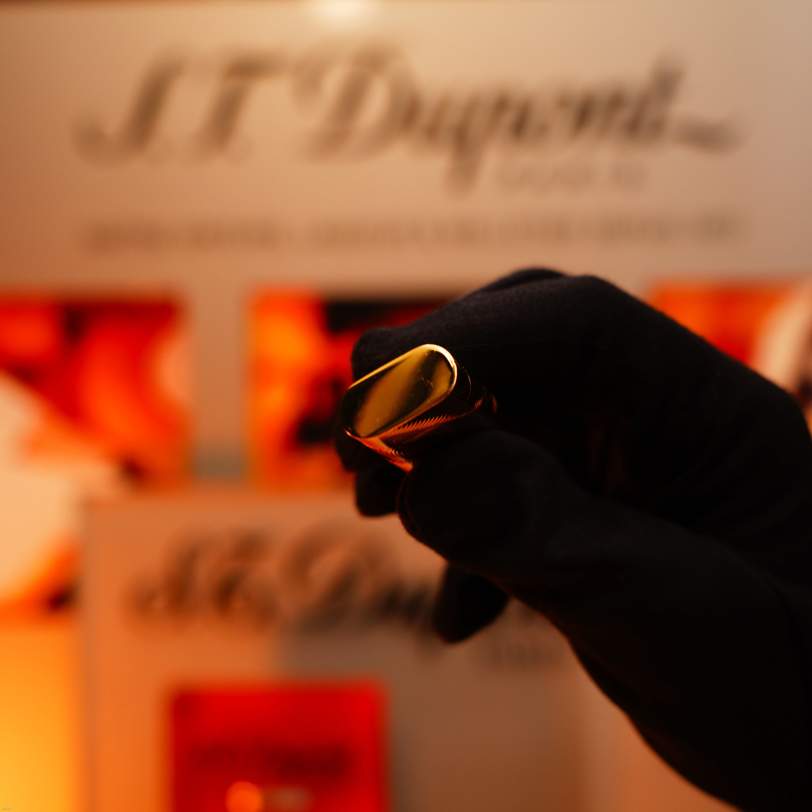 A gloved hand holds a vintage 1970 Cartier extremely rare solid 18K gold, heavy guilloché pattern, 750 hallmarked lighter by Lucy Lighter; the background features a blurred display.