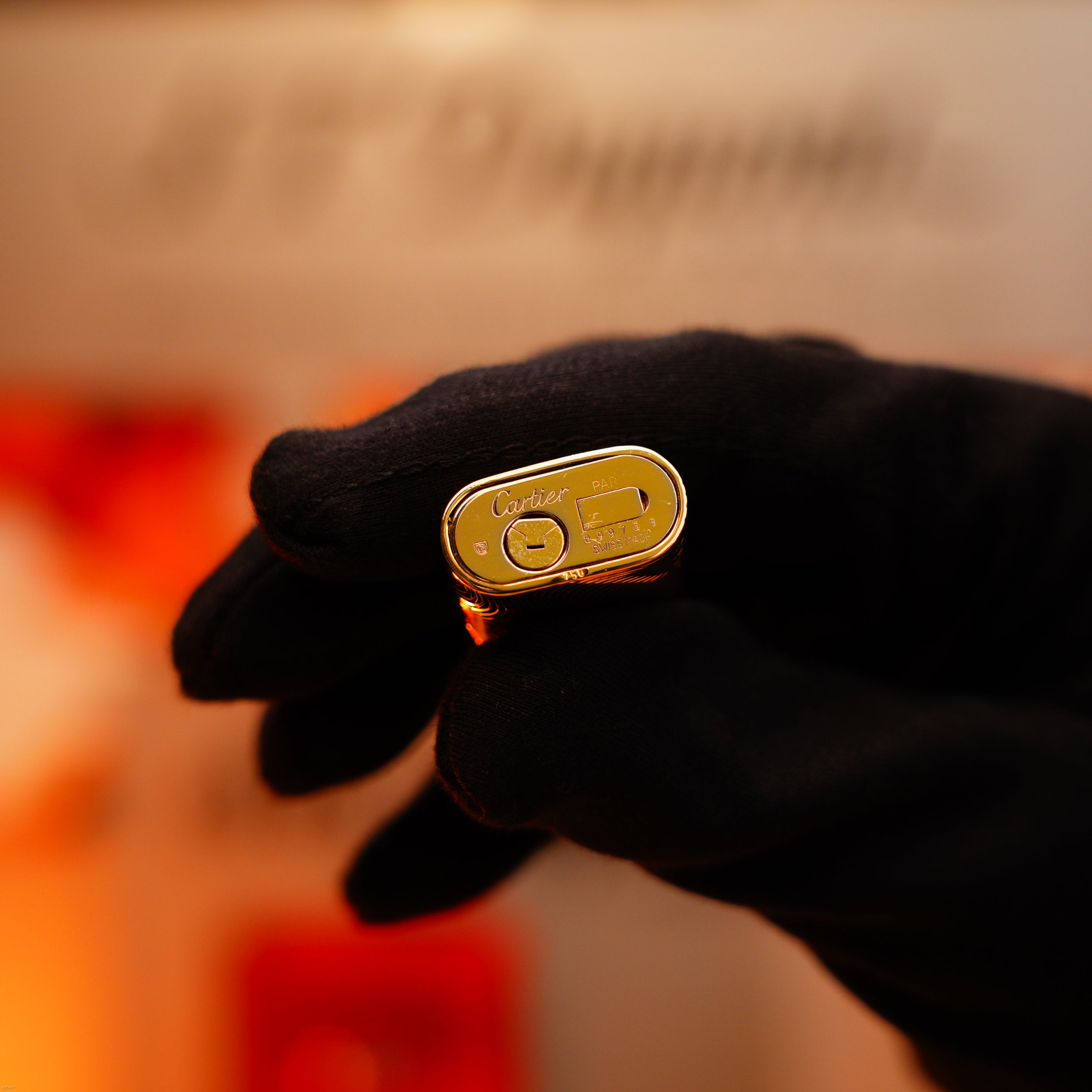A gloved hand holds a Vintage 1970 Lucy Lighter, an extremely rare solid 18K gold lighter with heavy guilloché pattern and 750 hallmark, displaying the engraved bottom.