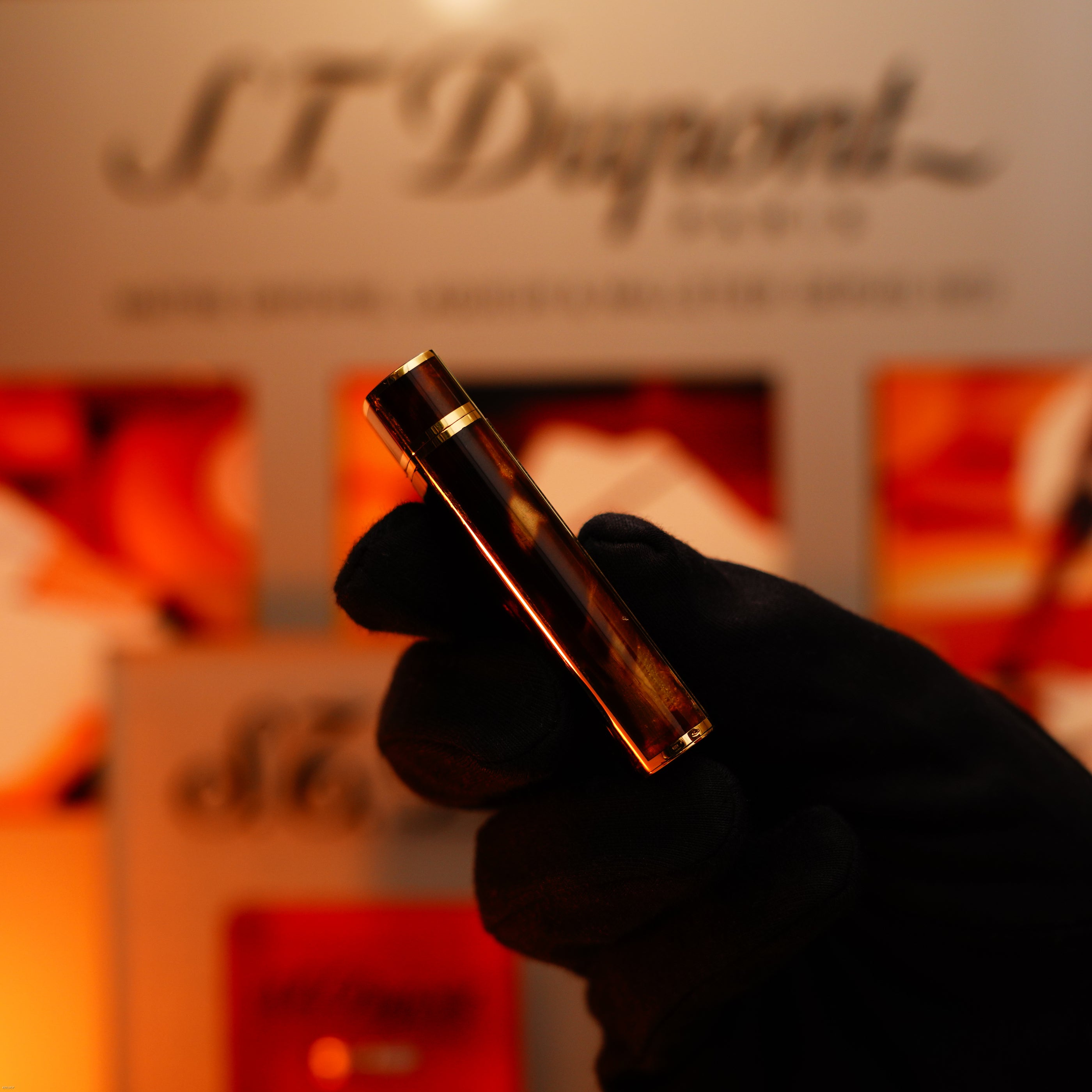 A gloved hand holds the Lucy Lighter Vintage 1970 Limited, an extremely rare solid 18K gold and tiger’s eye resin heavyweight lighter, in front of a blurred display with warm lighting, evoking ultimate luxury and exclusivity.
