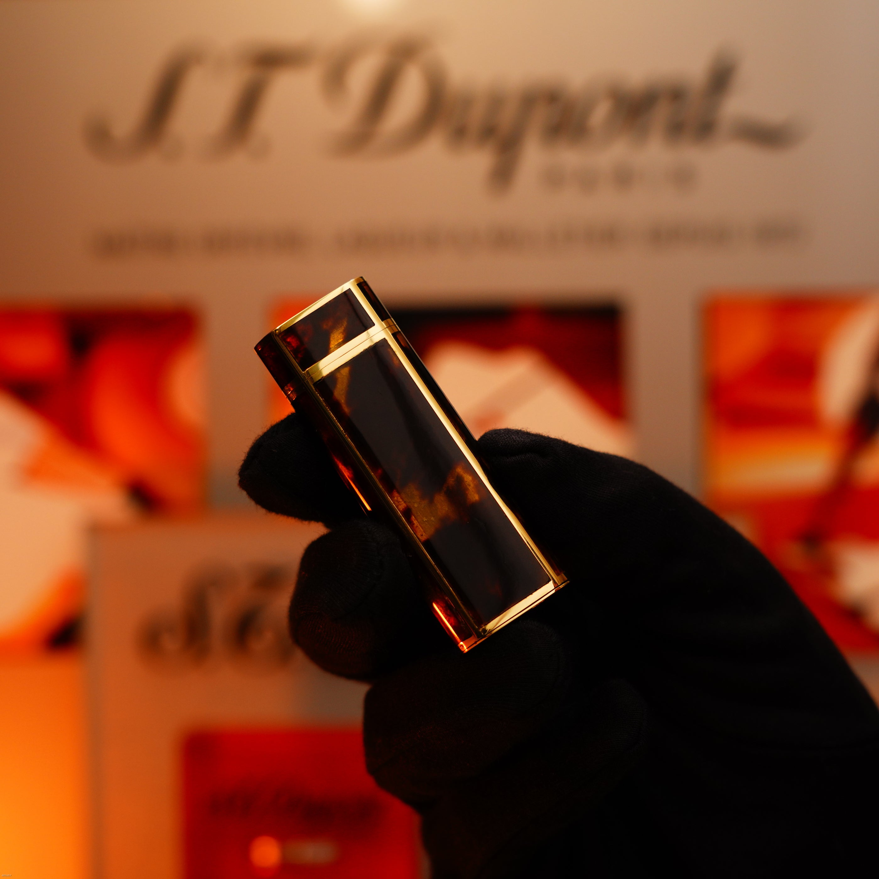 A gloved hand holds a Vintage 1970 Limited Cartier Extremely Rare Solid 18K Gold Tiger’s Eye Resin Lucy Lighter, with blurred signage and warm lighting in the background.