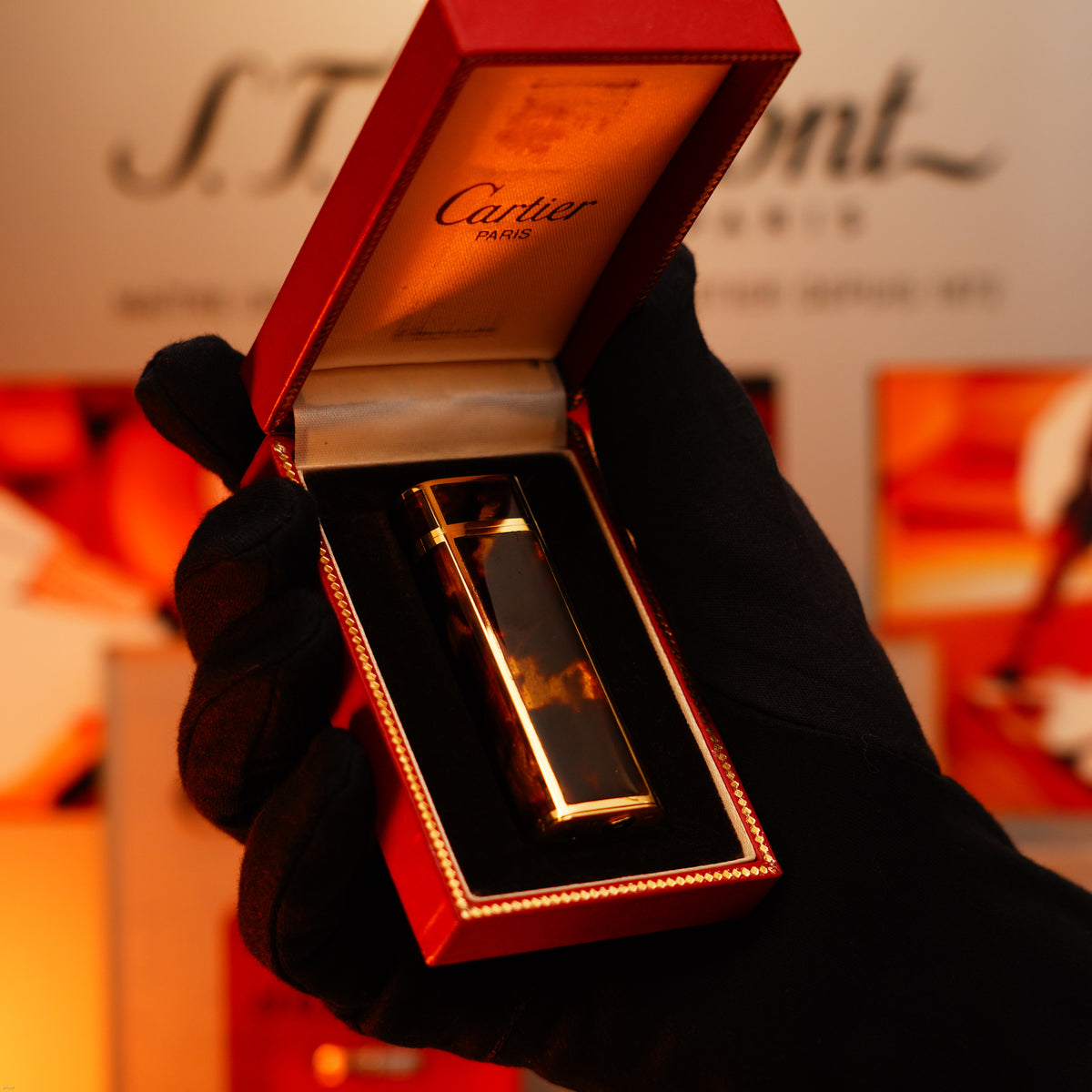 A gloved hand holds an open red box displaying the Lucy Lighter Vintage 1970 Limited Extremely Rare Solid 18K Gold and Tiger’s Eye Resin Lighter, Heavyweight, 750 Hallmarked 1/1, with a blurred background.