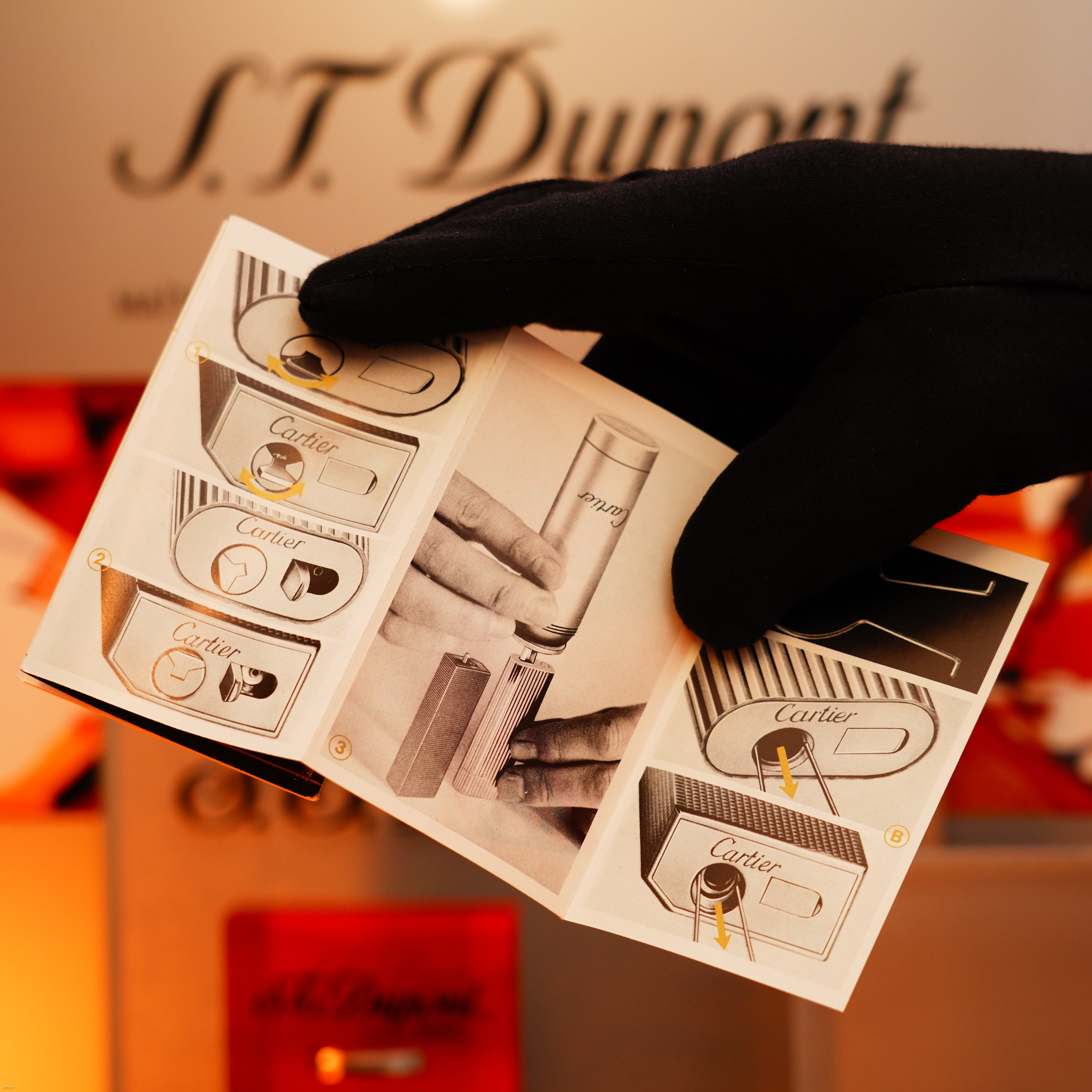 A gloved hand holds an instruction booklet with diagrams and photos for the Vintage 1970 Limited Cartier Extremely Rare Solid 18K Gold Tiger’s Eye Resin Lucy Lighter, set against a blurred background.