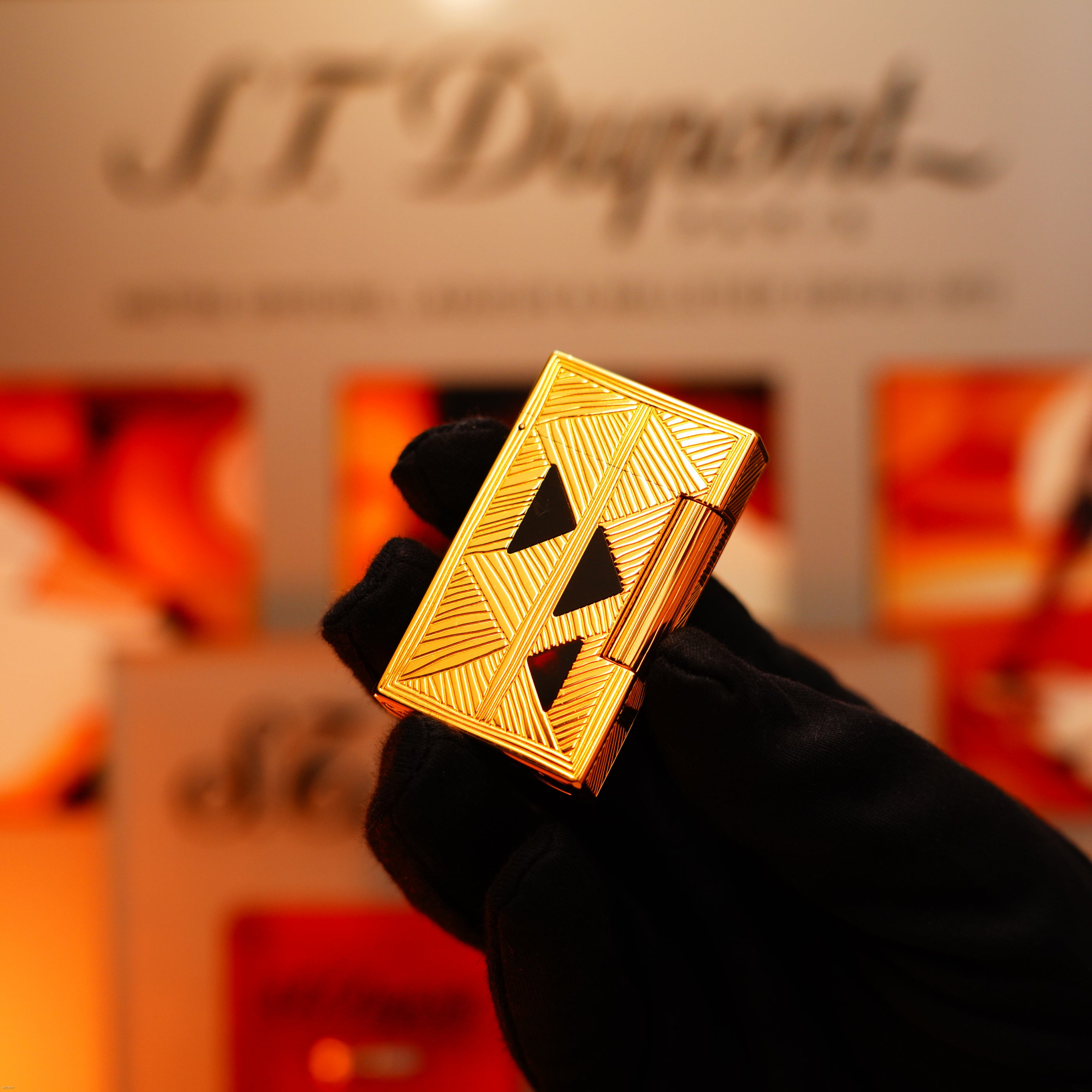 A gloved hand holds a Lucy Lighter Vintage 2000 St Dupont Limited Edition Heavy 24k Gold Finish Africa Natural Lacquer Large Ligne 2 Lighter against a blurred branded background.
