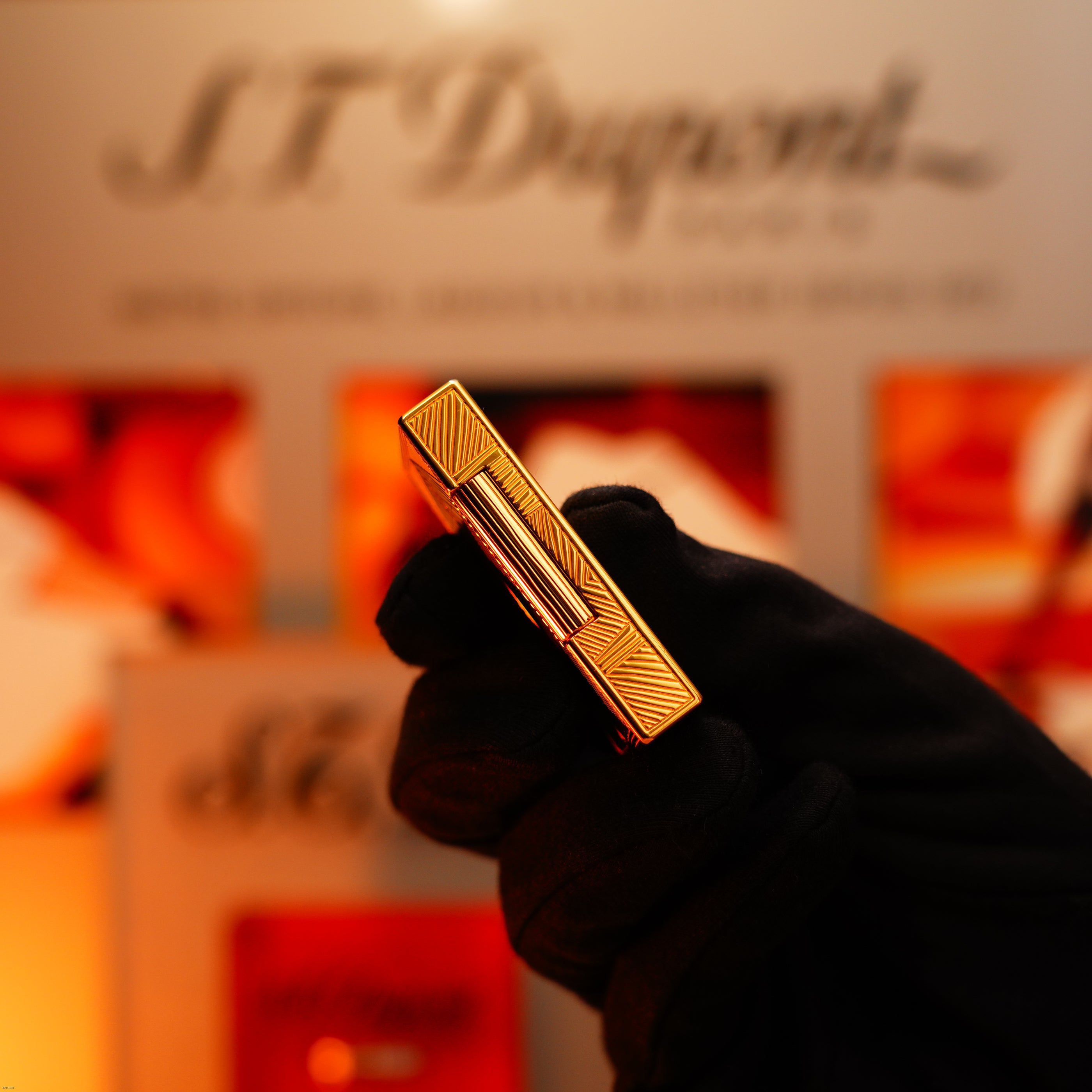 A gloved hand holds a Lucy Lighter Vintage 2000 Limited Edition Heavy 24k Gold Finish Africa Natural Lacquer Large Ligne 2 Lighter; a blurred logo and display in the background highlight its quality guarantee.