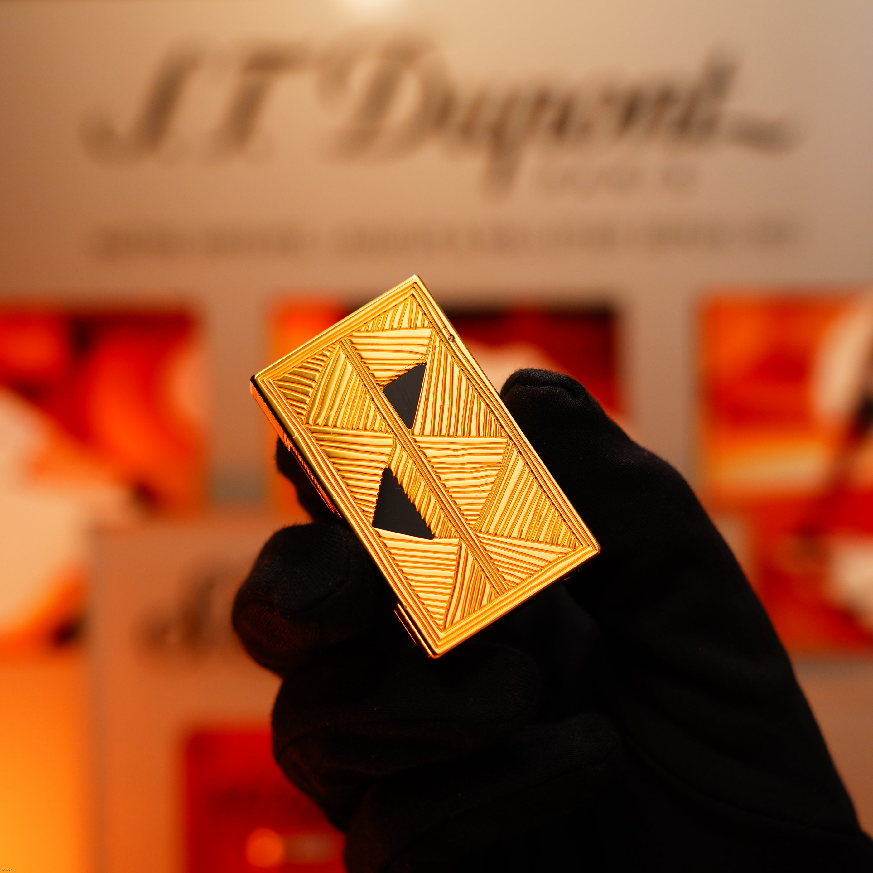 A gloved hand holds the Vintage 2000 St Dupont Limited Edition Heavy 24k Gold Finish Africa Natural Lacquer Large Ligne 2 Lighter by Lucy Lighter, its gold geometric design shown against a blurred background with "S.T. Dupont" text.