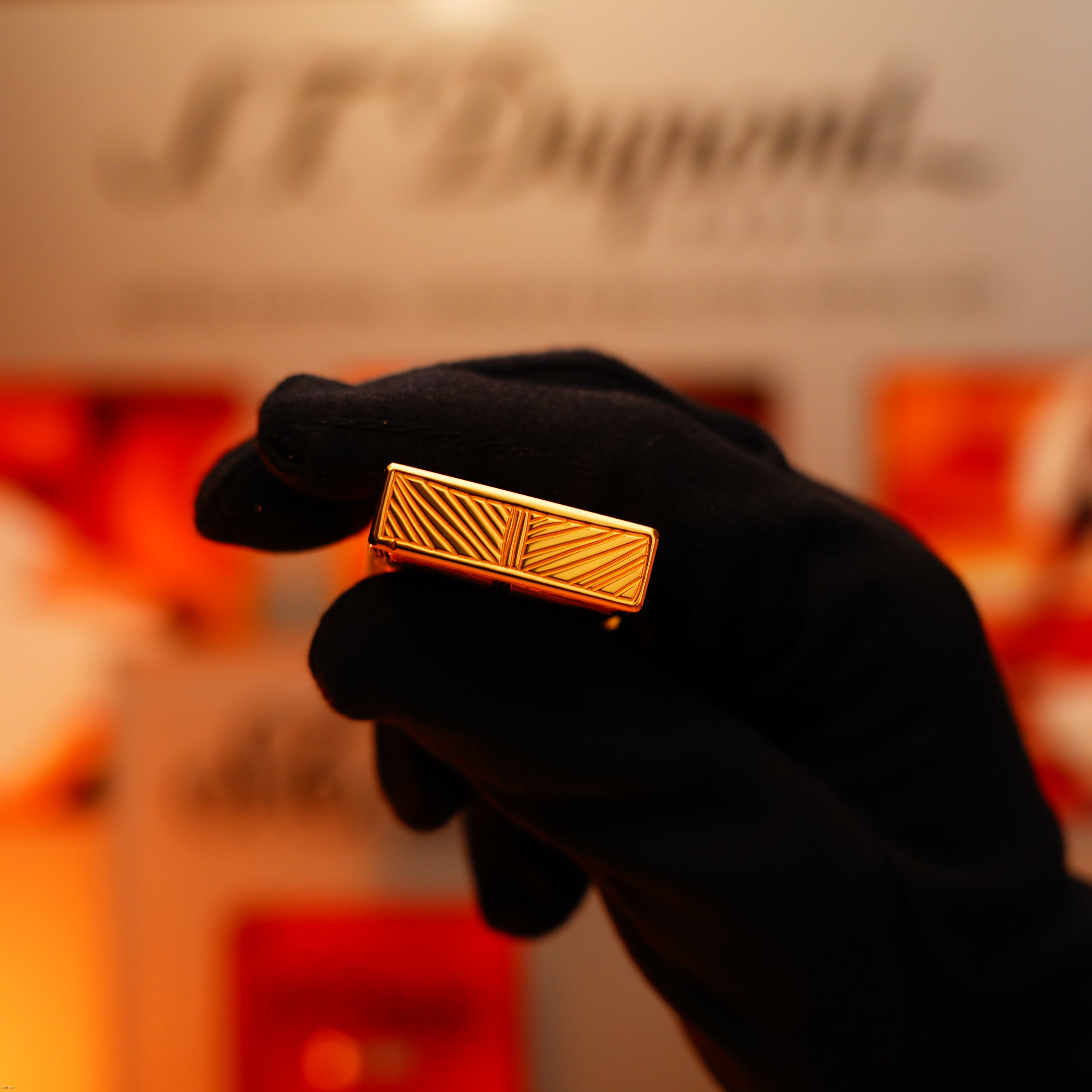 A gloved hand holds a Vintage 2000 St Dupont Limited Edition Heavy 24k Gold Finish Africa Natural Lacquer Large Ligne 2 Lighter by Lucy Lighter, with engraved lines, set against a blurred background featuring the S.T. Dupont logo.