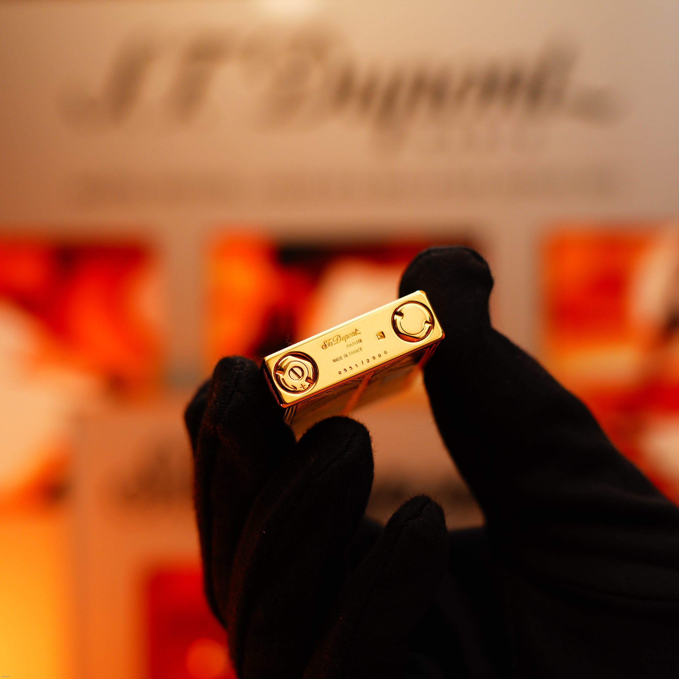 A gloved hand holds a Lucy Lighter Vintage 2000 Limited Edition Heavy 24k Gold Finish Africa Natural Lacquer Large Ligne 2 lighter close to the camera, highlighting its luxurious design and collectible appeal.