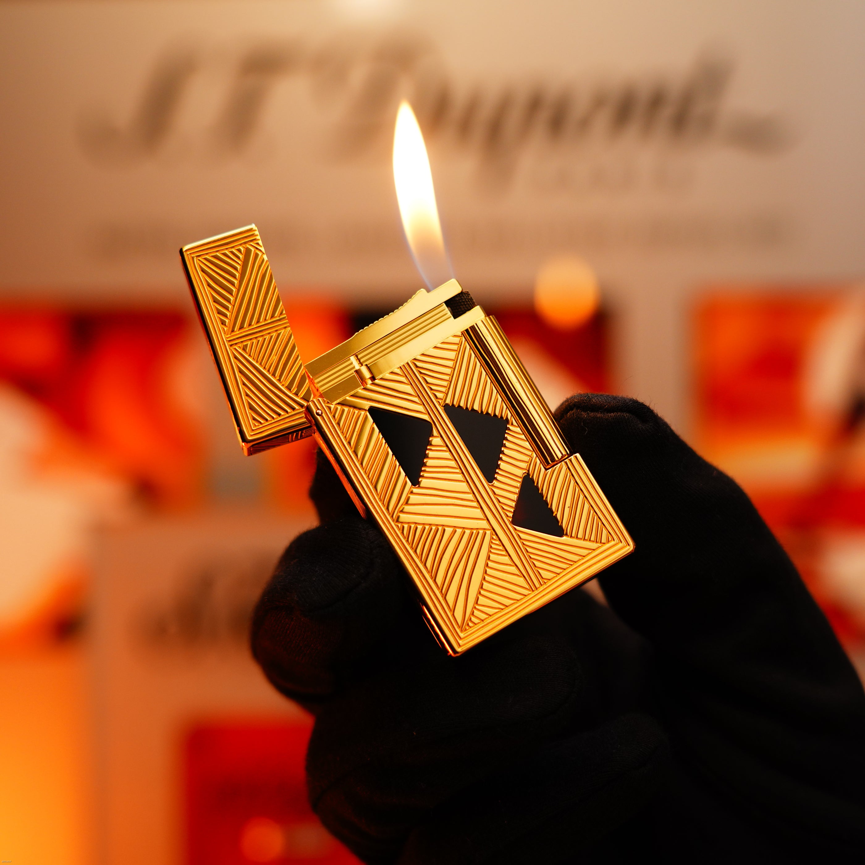 A gloved hand holds a lit Lucy Lighter Vintage 2000 St Dupont Limited Edition Heavy 24k Gold Finish Africa Natural Lacquer Large Ligne 2; blurred background.