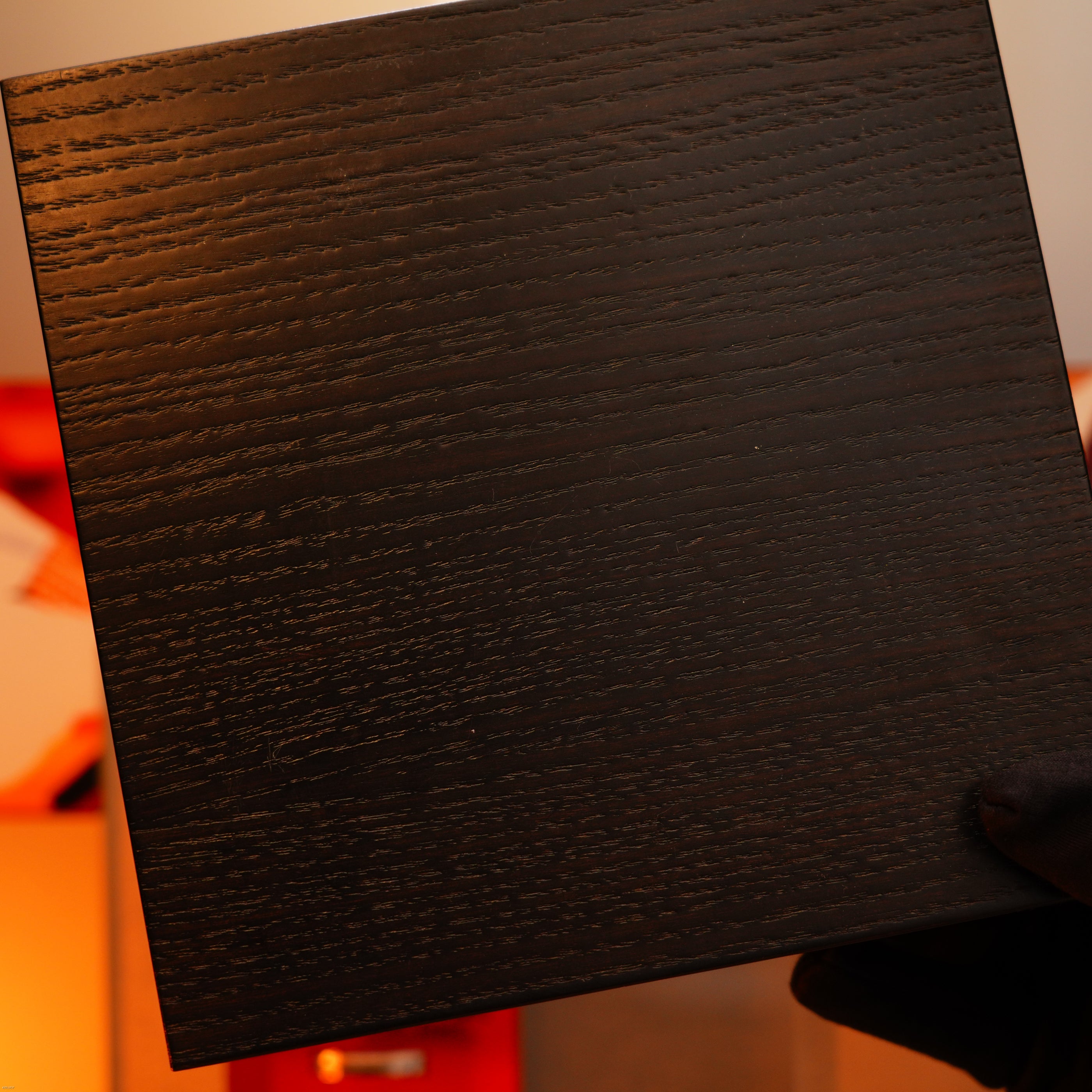 A gloved hand holds up a Lucy Lighter Vintage 2000 St Dupont Limited Edition Heavy 24k Gold Finish Africa Natural Lacquer Large Ligne 2 Lighter, its dark wood grain pattern evoking luxury against a blurred indoor background.