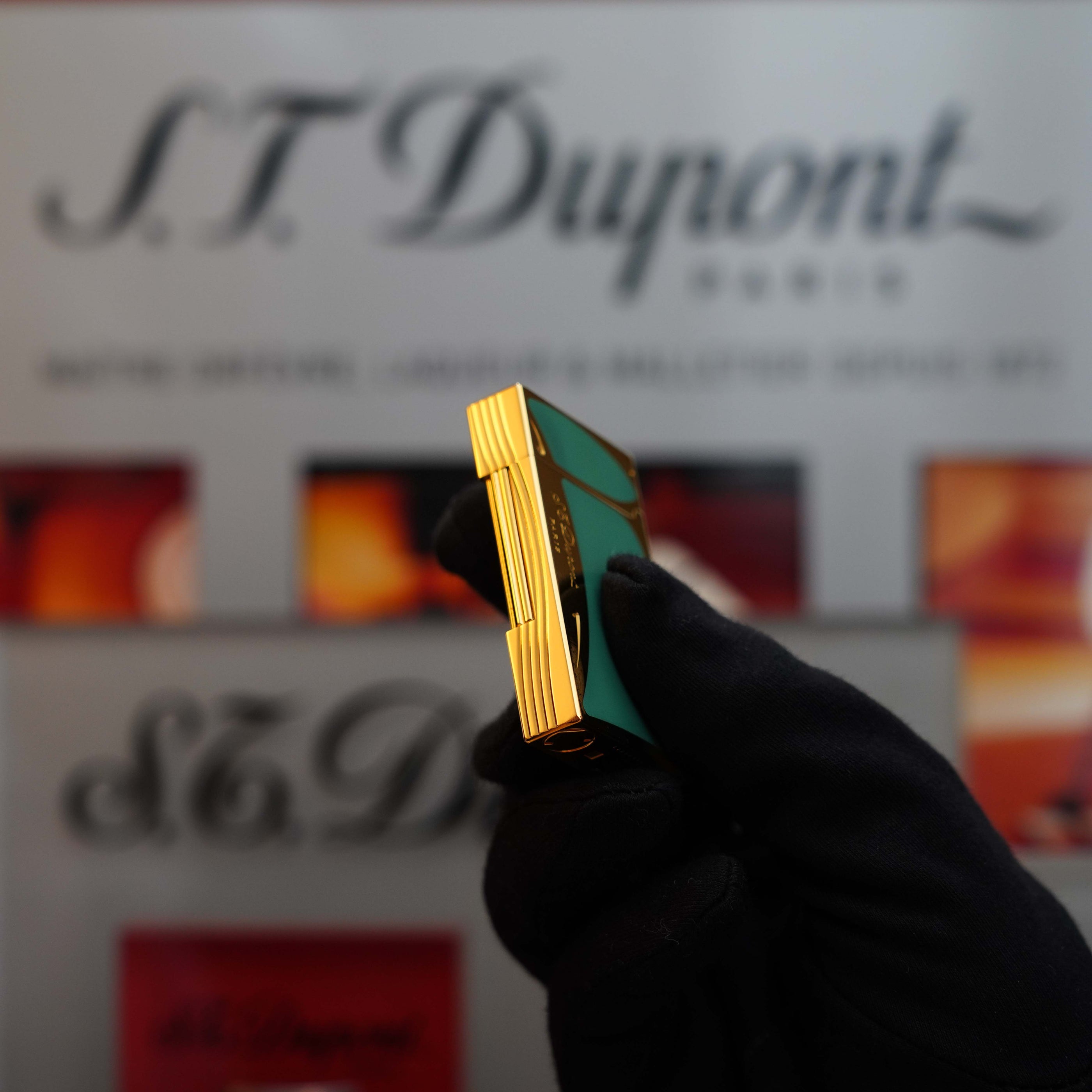 A gloved hand holds a Vintage 1993 rare Art Nouveau early Limited Editions 24k Gold finish natural Green lacquer ligne 2 lighter with a green and 24k gold finish, against a blurred background featuring the S.T. Dupont brand name.