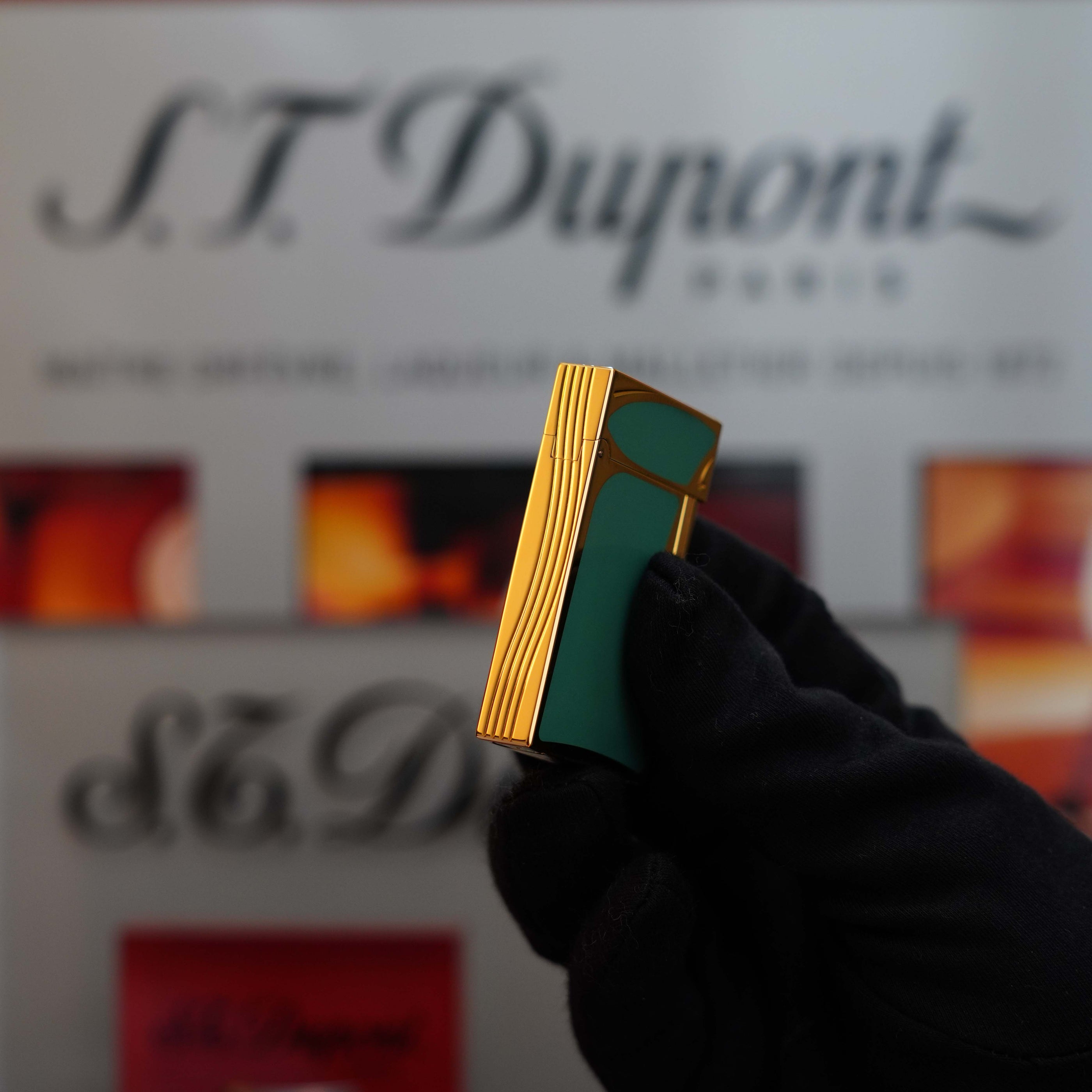 A gloved hand holds a Vintage 1993 rare Art Nouveau early Limited Editions 24k Gold finish natural Green lacquer ligne 2 lighter from S.T. Dupont. The brand's name is displayed in the blurred background.