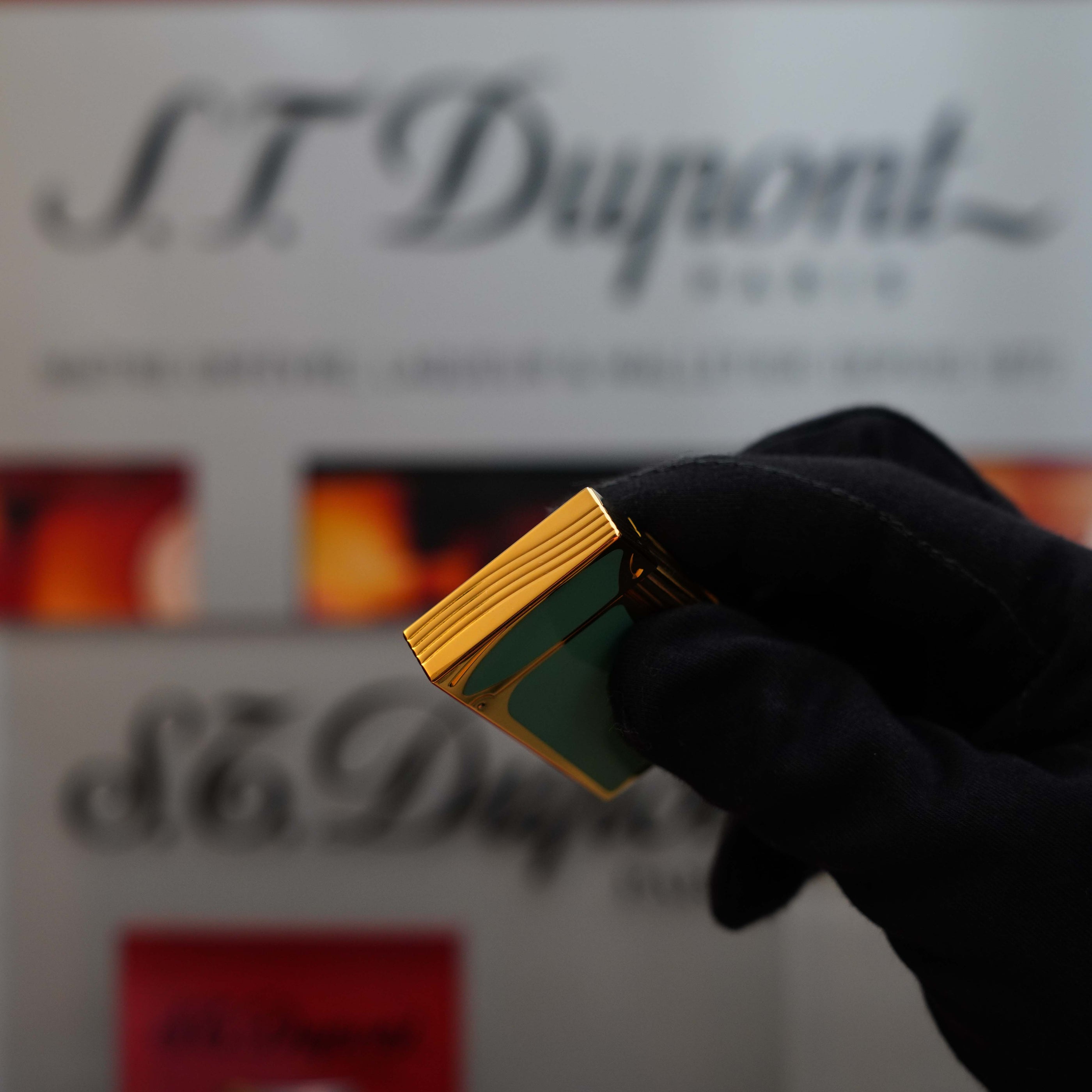 A gloved hand holds a gold and green Vintage 1993 rare Art Nouveau early Limited Editions 24k Gold finish natural Green lacquer ligne 2 lighter from S.T. Dupont in front of a blurred S.T. Dupont display background, showcasing the elegance of St Dupont Limited Editions.