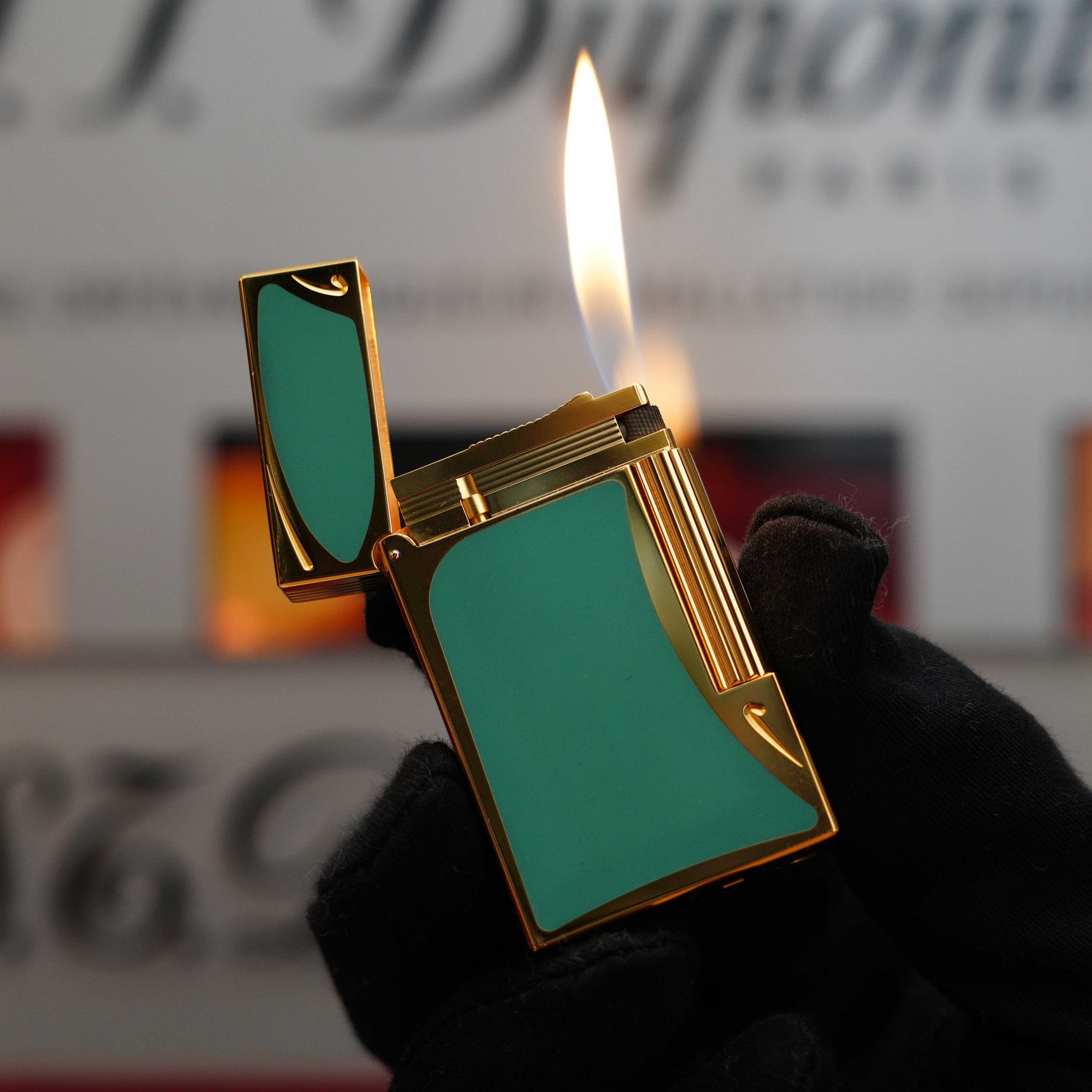 A gloved hand holds a lit S.T. Dupont Vintage 1993 rare Art Nouveau early Limited Editions 24k Gold finish natural Green lacquer ligne 2 lighter against a blurred background.