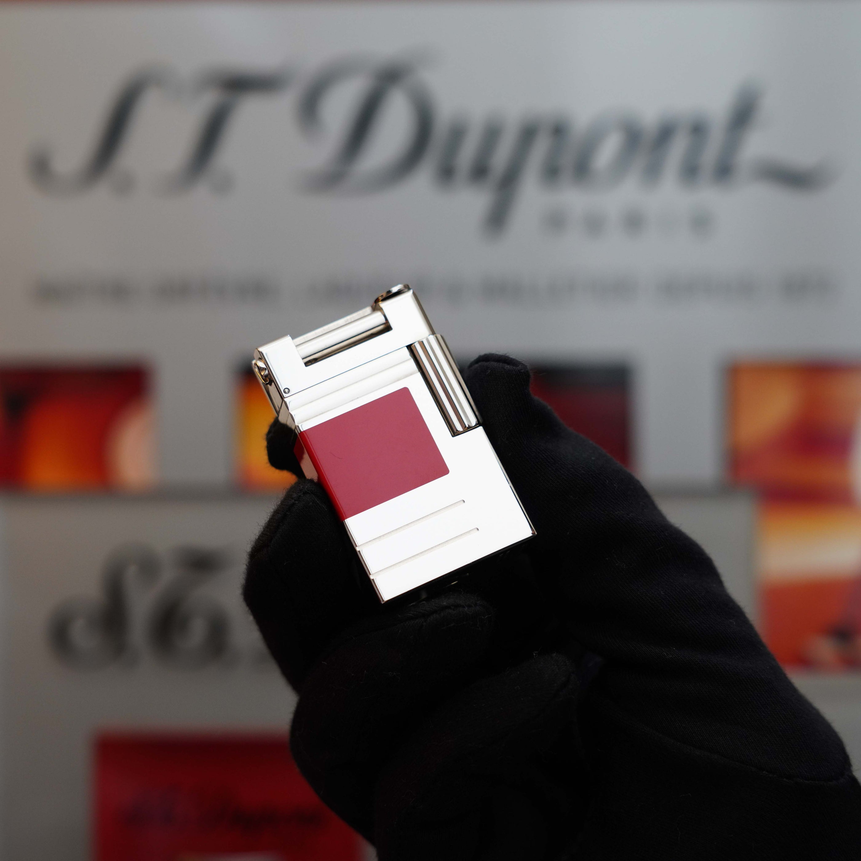 A gloved hand holds a Vintage 1999 S.T. Dupont Urban Limited Edition Platinum finish natural Red Lacquer lighter with a red and white design, an Urban Limited Edition that stands out prominently. The S.T. Dupont brand name is visible in the background, making this piece a must-have collector's item.