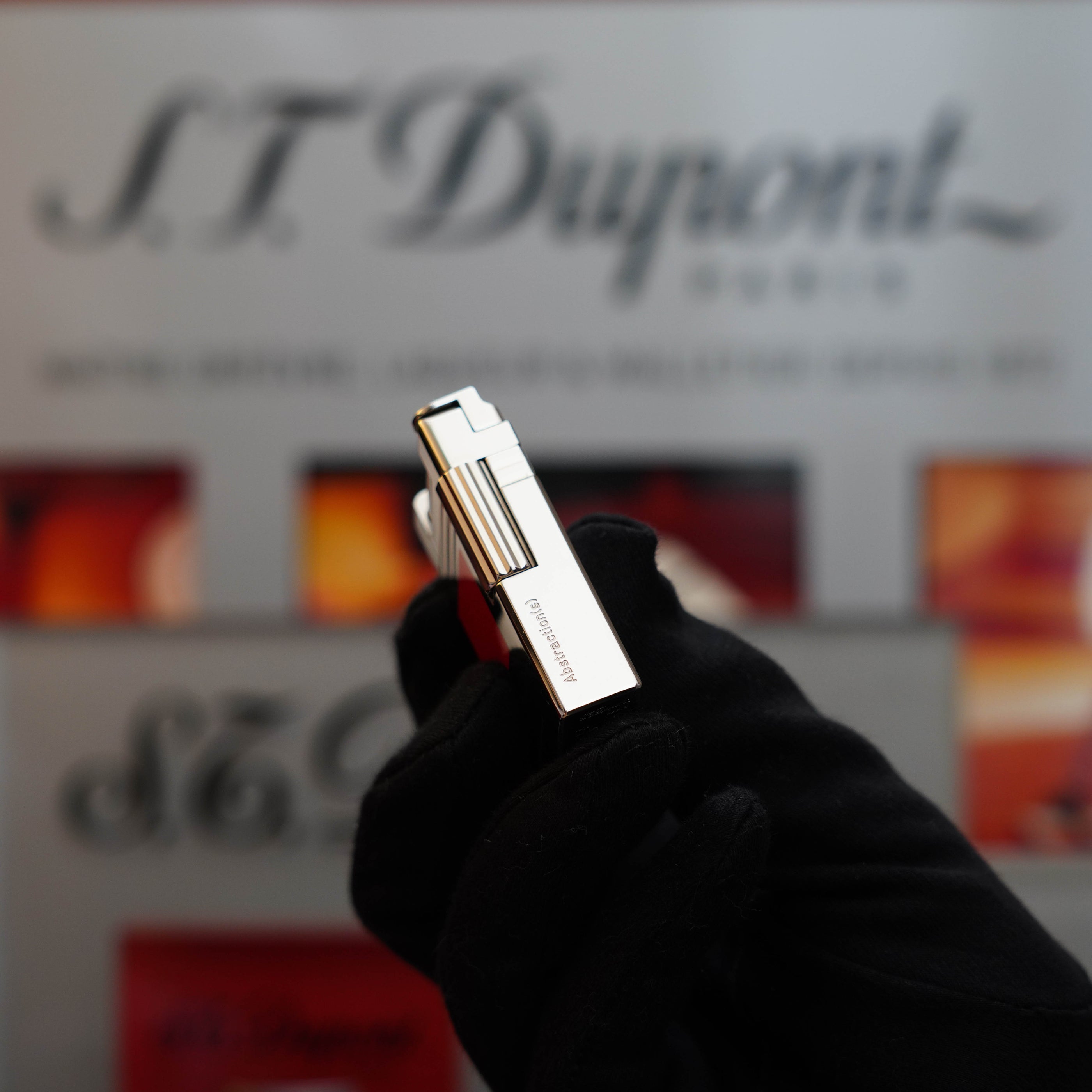 A gloved hand holding a Vintage 1999 S.T. Dupont Urban Limited Edition Platinum finish natural Red Lacquer lighter in front of a display with the brand's logo, showcasing a true collector's item.