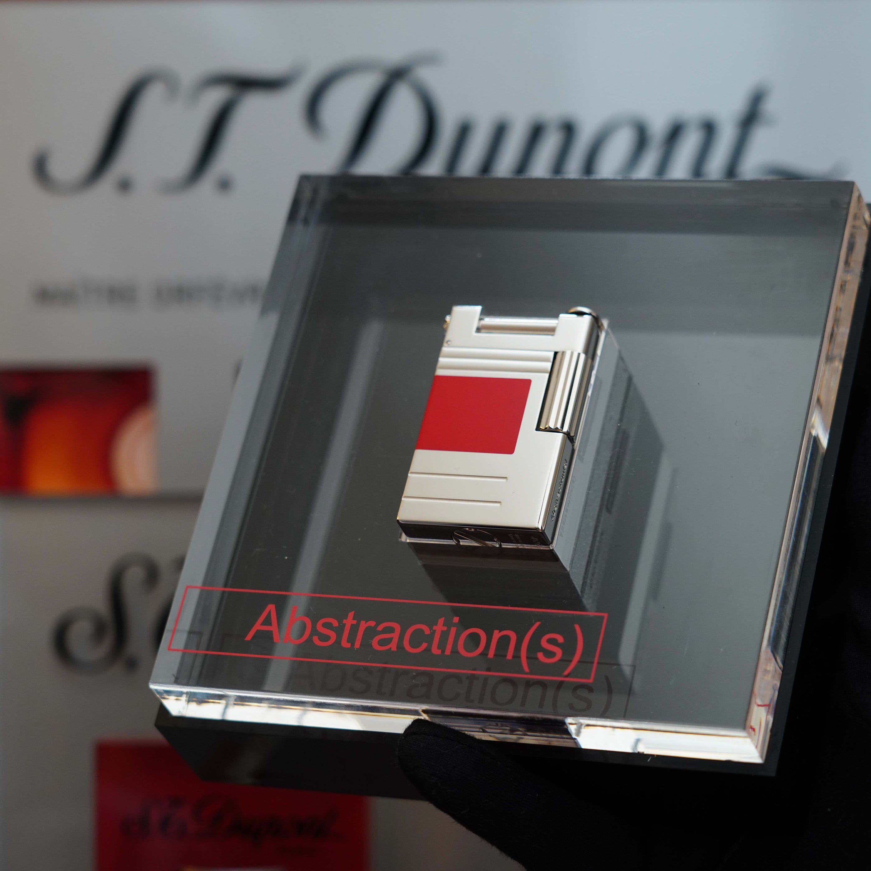 A silver rectangular object with a red square detail is displayed inside a clear box labeled "Vintage 1999 St Dupont Urban Limited Edition Platinum finish natural Red Lacquer lighter" with the S.T. Dupont brand name in the background, offering a striking Urban Limited Edition that is sure to be a prized collector's item.