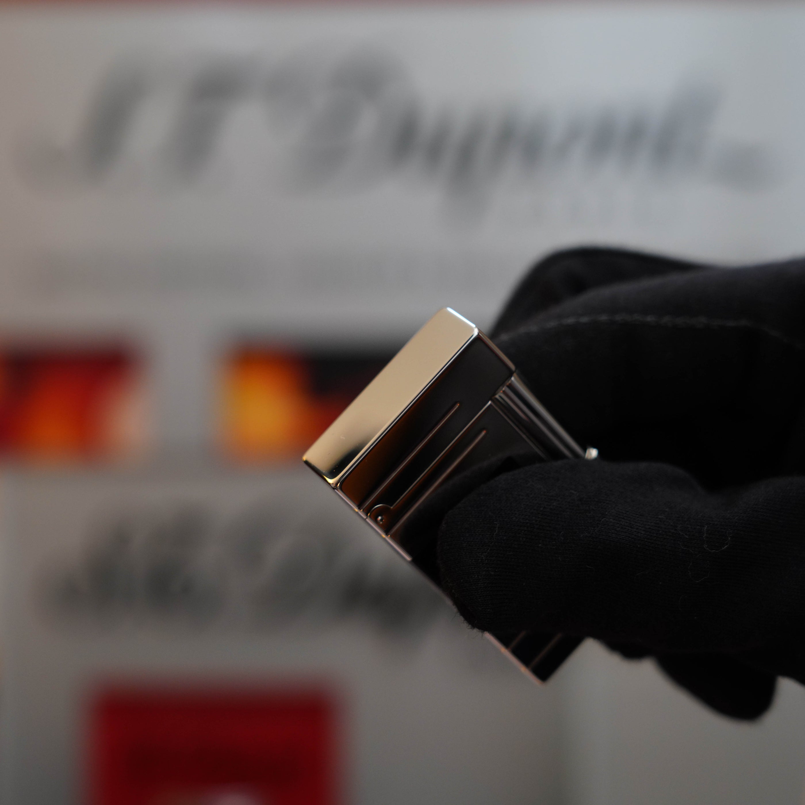 A gloved hand holding a Vintage 1999 S.T. Dupont Ligne 1 Limited Edition Platinum finish natural Black Lacquer lighter with blurred background branding.