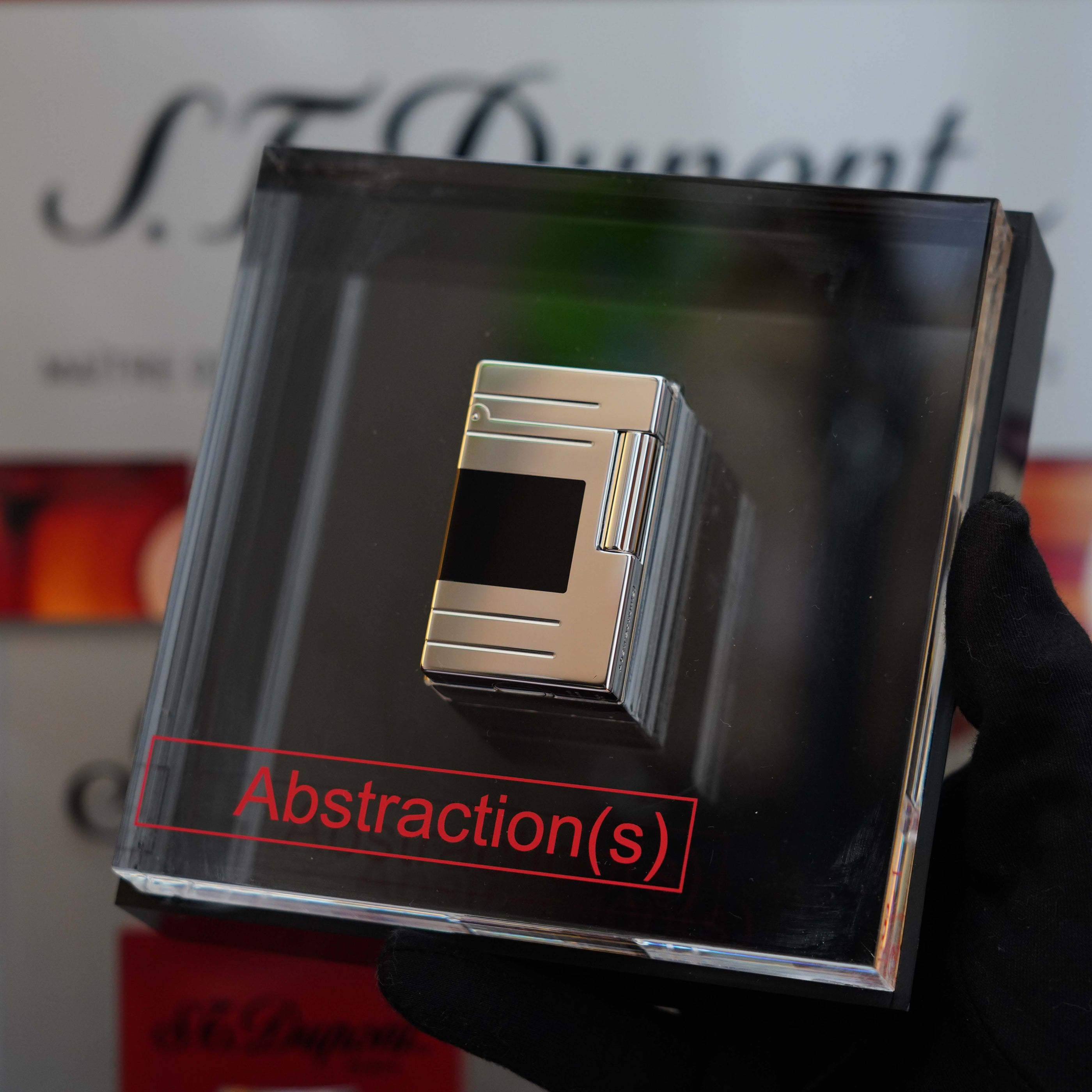 A person wearing a black glove holds a Vintage 1999 St Dupont Ligne 1 Limited Edition Platinum finish natural Black Lacquer lighter encased in a clear box labeled "S.T. Dupont.