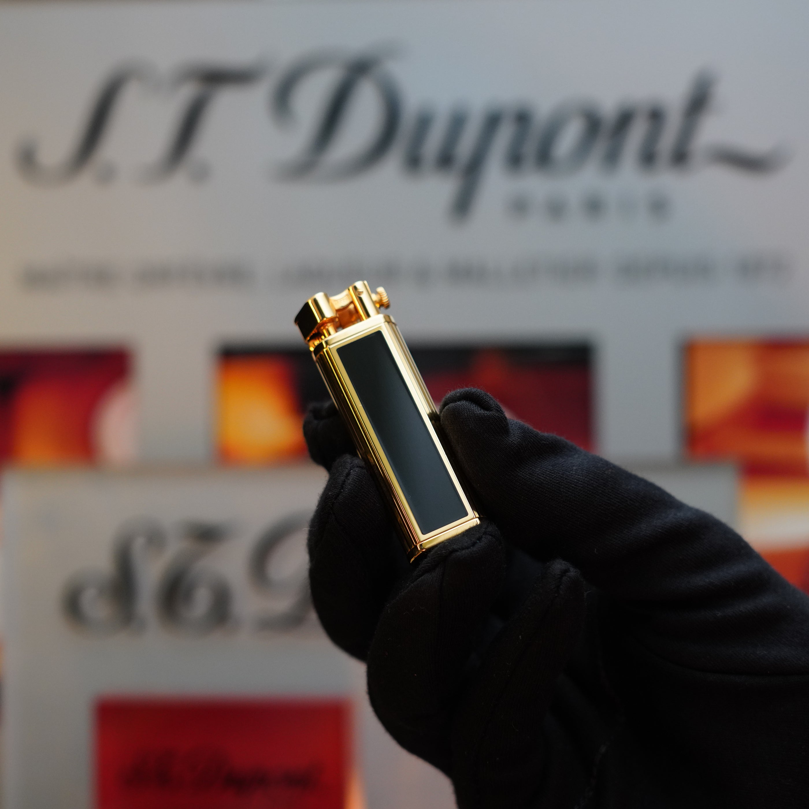 A gloved hand holds a 1980 Dunhill Unique Sylfide 24k Heavy Gold Natural Lacquer lighter, with its vintage luxury gold and black design, while the Dunhill branding is visible in the background.