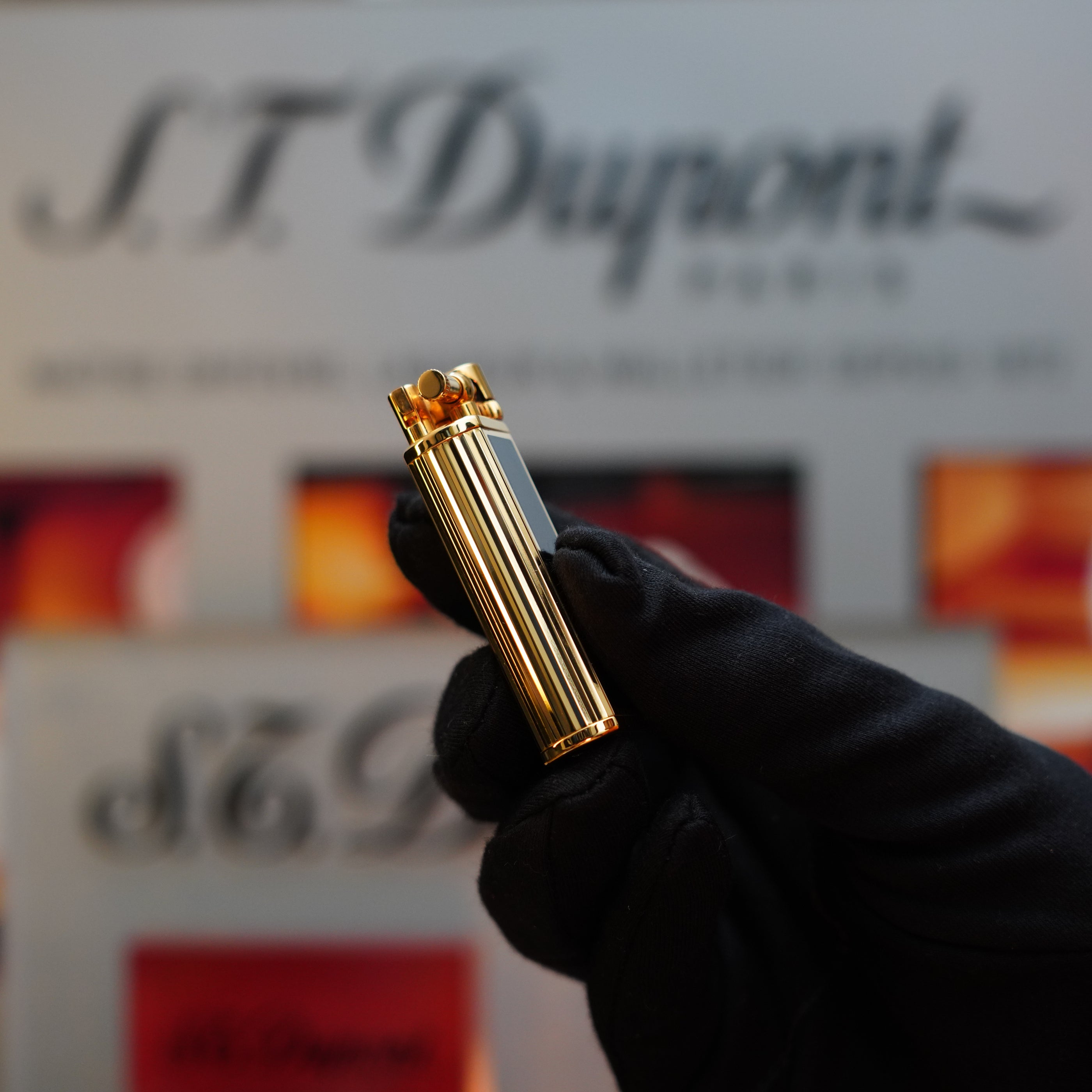 A gloved hand holds a vintage Dunhill 1980 Unique Sylfide lighter, elegantly crafted with heavy 24k gold and natural lacquer, against a black background with blurred branding.