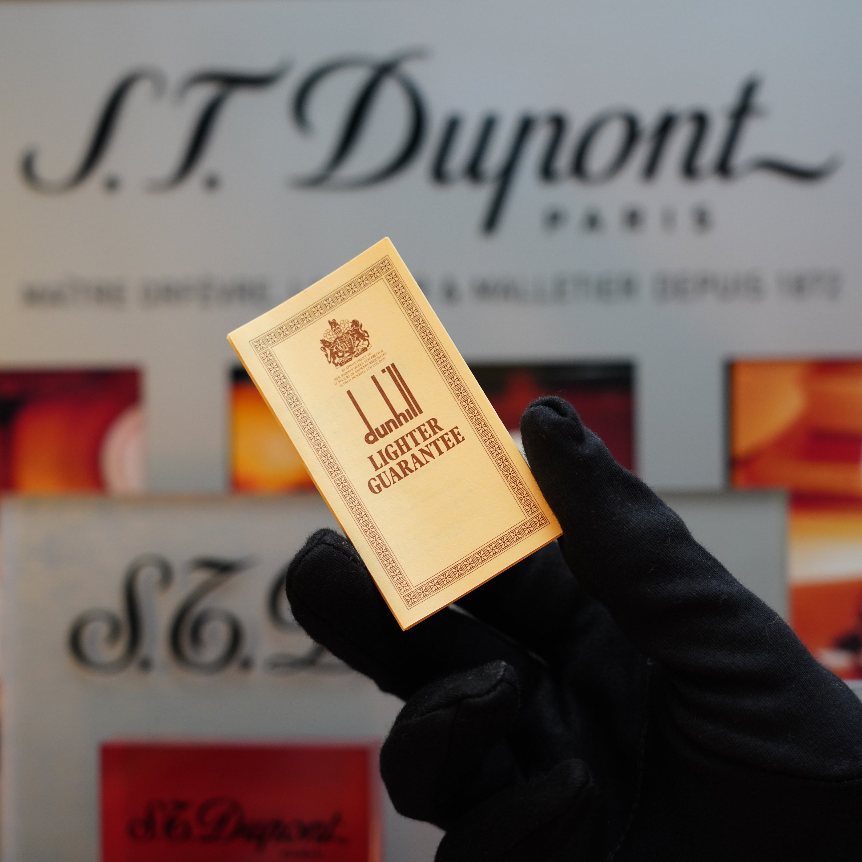 A gloved hand holds a silver 1970 Dunhill Rollagas Vertical Line Heavy Finish Lighter with the text "Lighter Guarantee" against a background featuring the Dunhill logo—a true collector's item for those who appreciate luxury and craftsmanship.