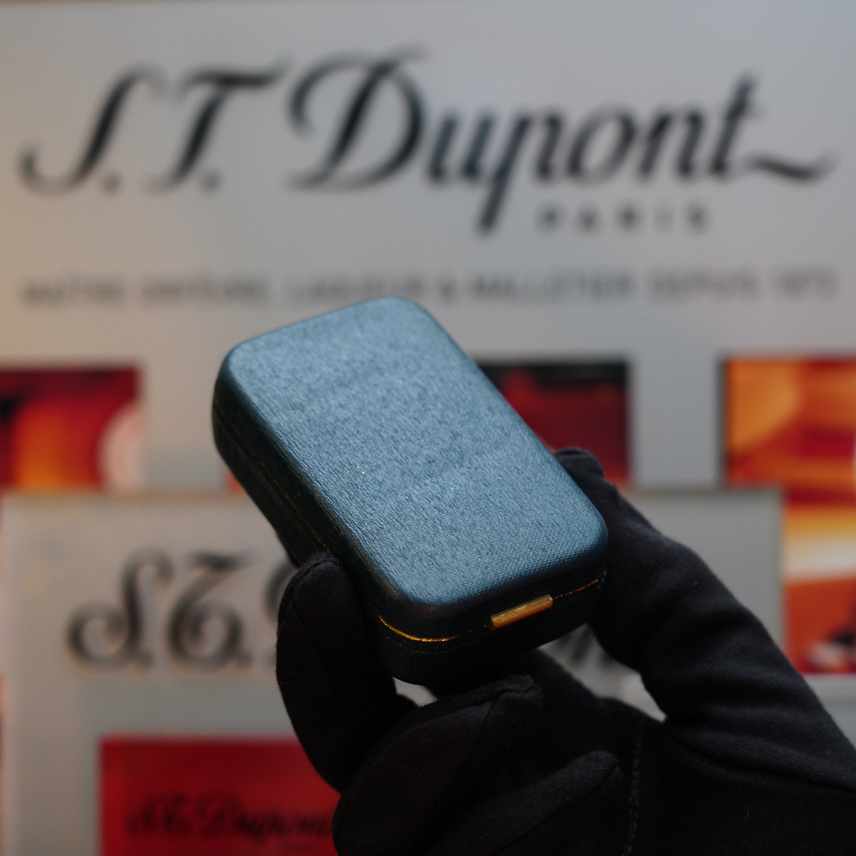 A gloved hand holds a 1970 Dunhill Rollagas Vertical Line Heavy Silver Finish Lighter in front of a blurred Dunhill sign.