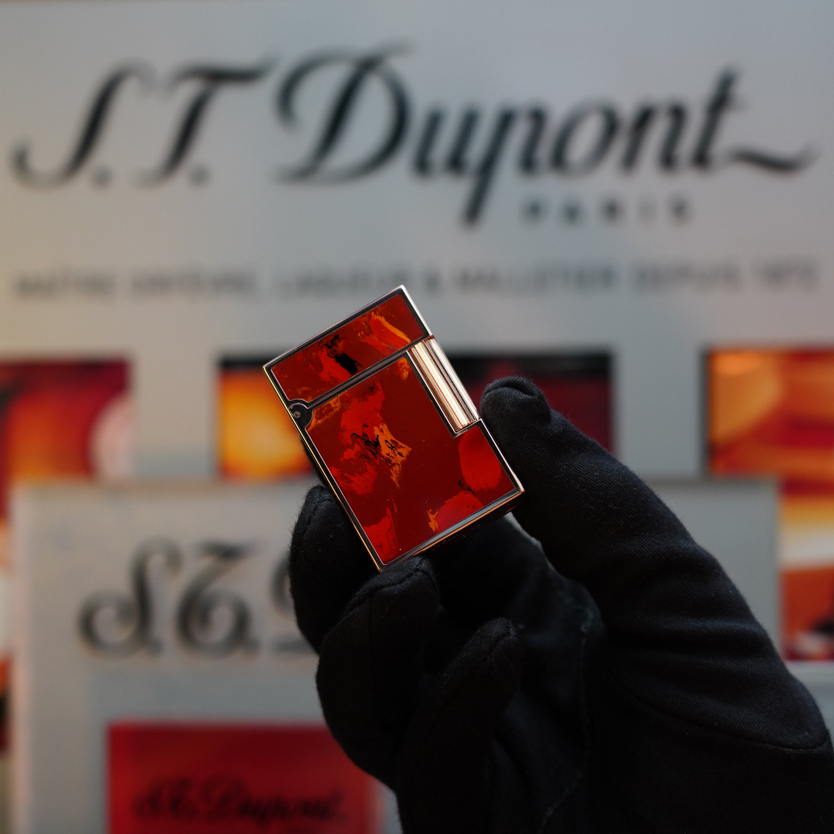 A gloved hand holding a rare 1970 S.T. Dupont Picaso 24k Rose Gold Ligne 2 Natural Lacquer lighter against a blurred background with the S.T. Dupont logo, showcasing this exquisite collector's item.