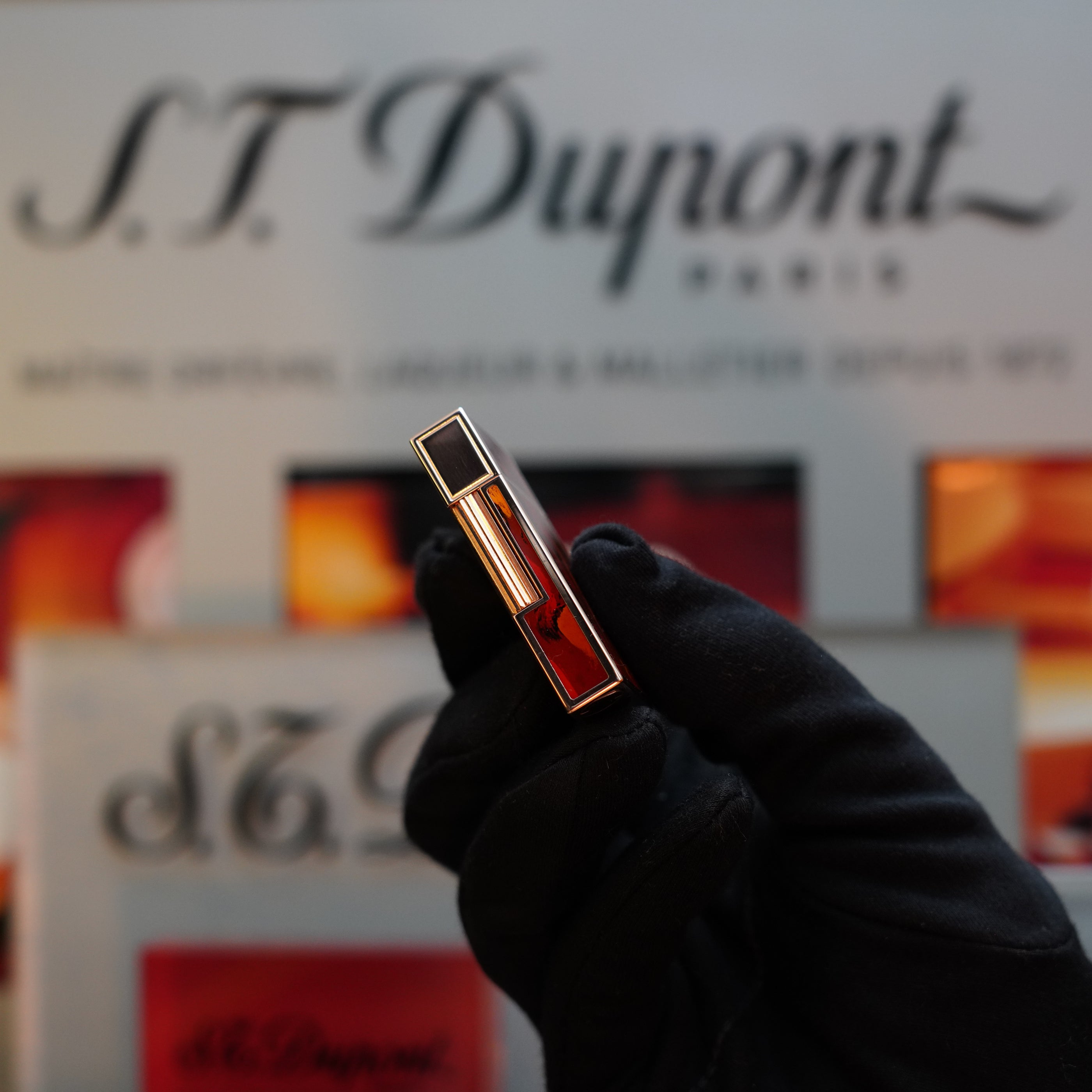 A gloved hand holds a sleek, rectangular 1970 St Dupont Picaso 24k Rose Gold Ligne 2 Natural Lacquer rarer lighter against a blurred background displaying S.T. Dupont branding.