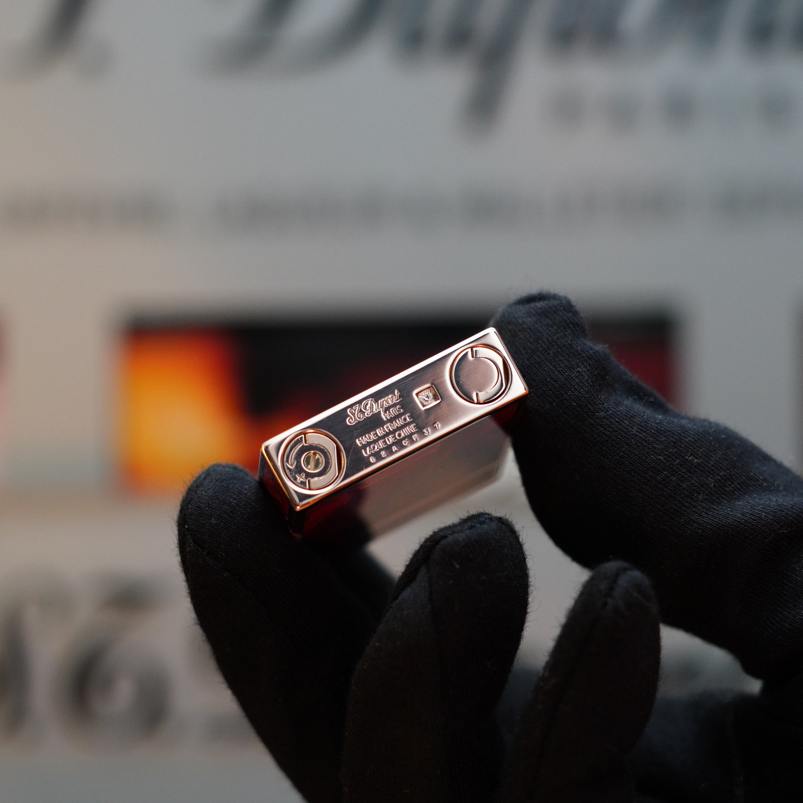 A gloved hand holding a 1970 S.T. Dupont Picasso 24k Rose Gold Ligne 2 Natural Lacquer lighter with engraved details on its surface, pictured against a blurred background—truly a collector's item.