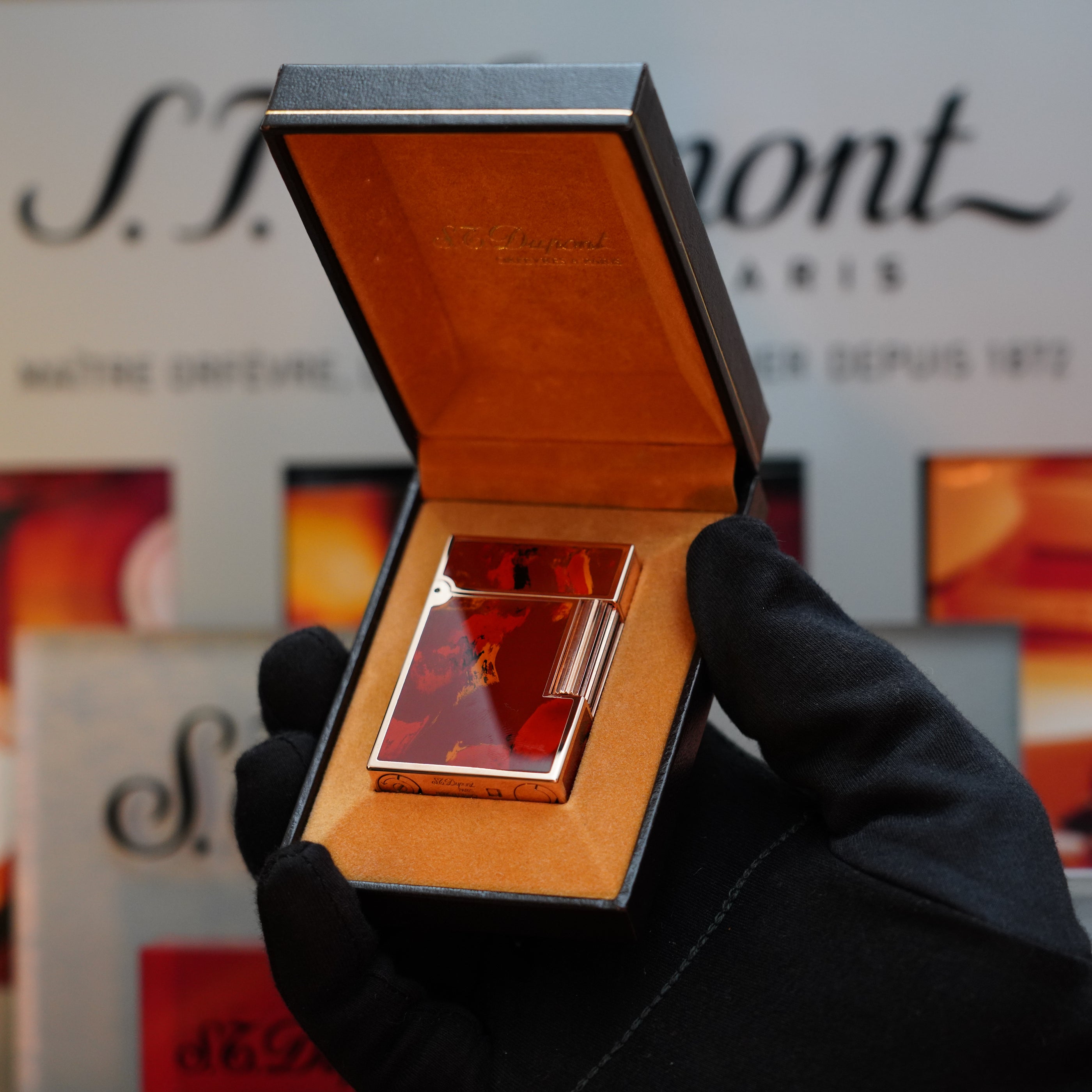 A gloved hand holds an open box displaying a rare 1970 St Dupont Picasso 24k Rose Gold Ligne 2 Natural Lacquer lighter against a background with the brand "S.T. Dupont" visible, making it a prized collector's item.