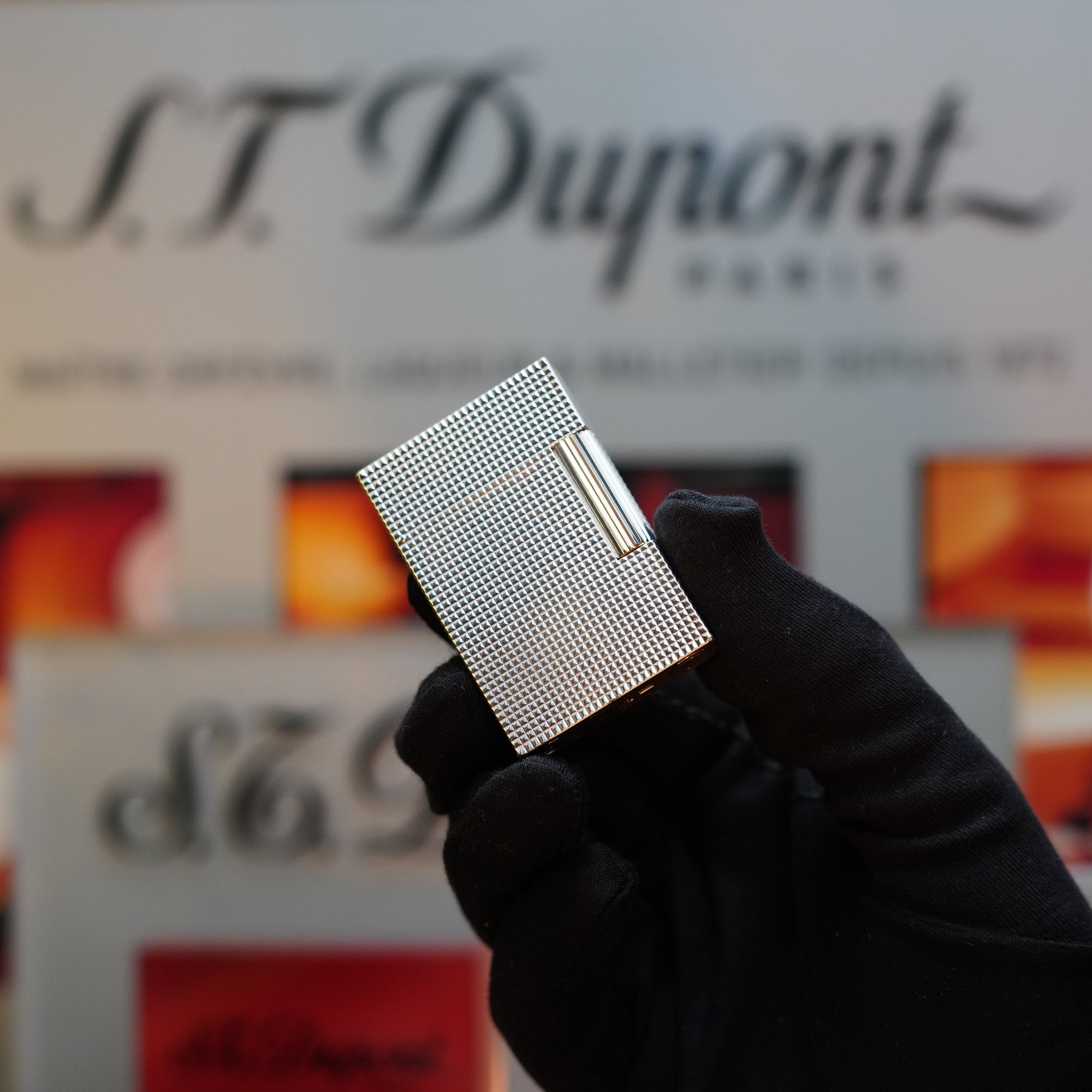 A gloved hand is holding the 1970 S.T. Dupont Diamond Head Lighter Heavy Silver Finish ligne 2, with S.T. Dupont branding visible in the background.