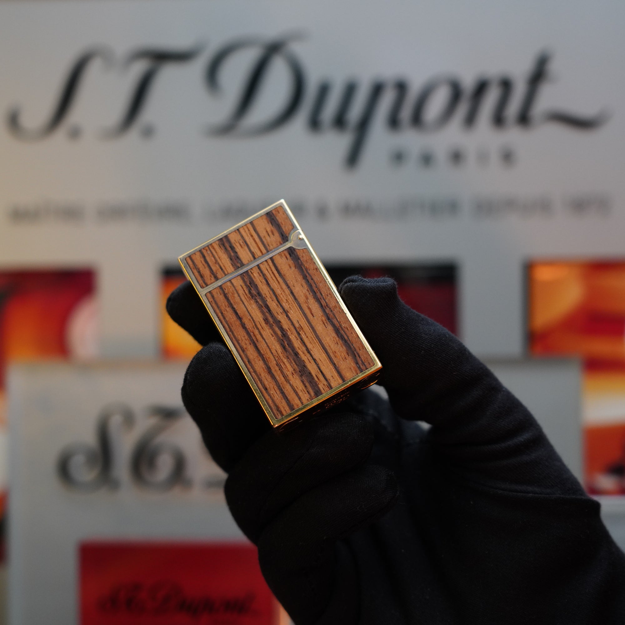 A person wearing a black glove is holding a 1989 S.T. Dupont Real Wood no lacquer, prototype, extremely rare Ligne 2 lighter. This vintage lighter, part of the Limited Prototype Series, has the S.T. Dupont logo visible in the blurred background.