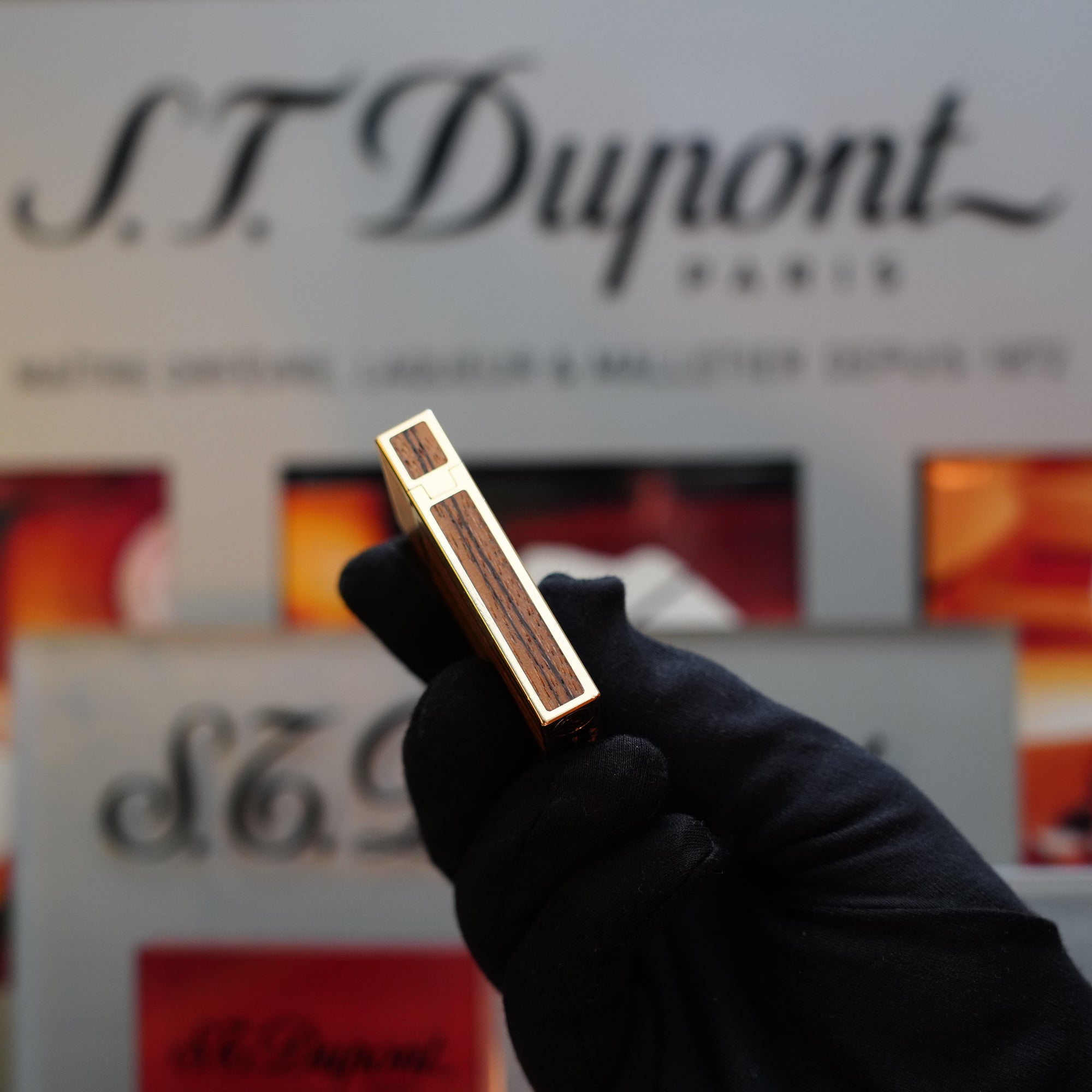 A hand in a black glove holds the 1989 S.T. Dupont Real Wood no lacquer, prototype, extremely rare Ligne 2 lighter. The background reveals an S.T. Dupont Paris sign, hinting at a coveted collector's item from the Limited Prototype Series.