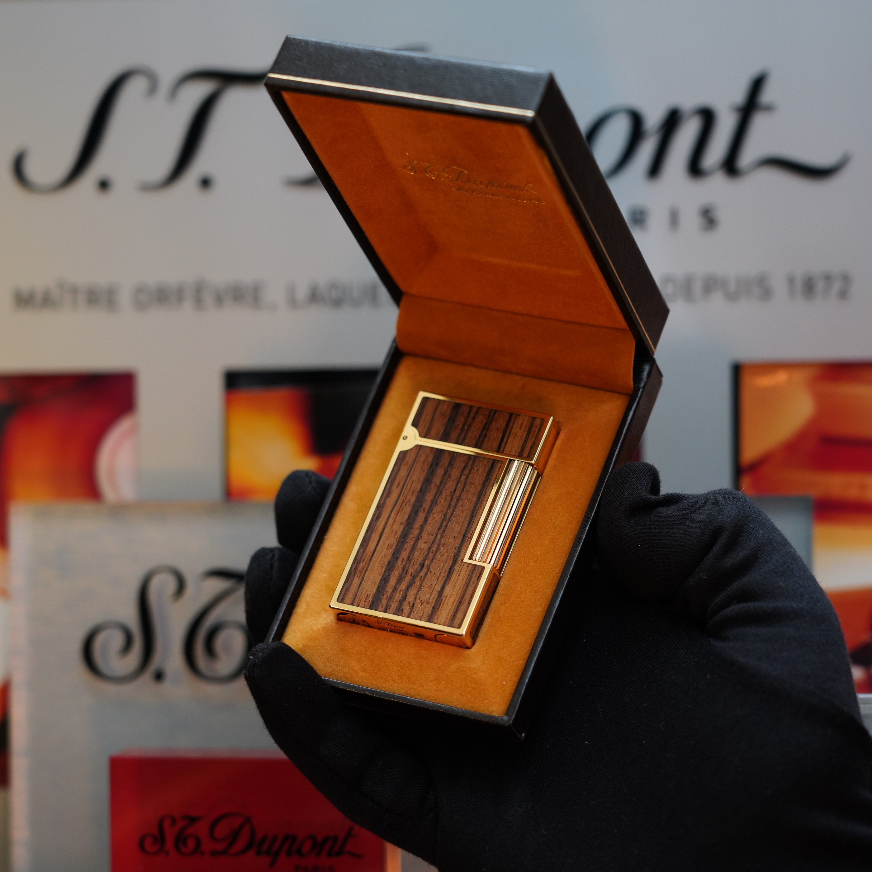 A gloved hand holds an open black box containing the 1989 St Dupont Real Wood no lacquer, prototype, extremely rare Ligne 2 lighter against a background featuring the S.T. Dupont logo - a true collector's item.