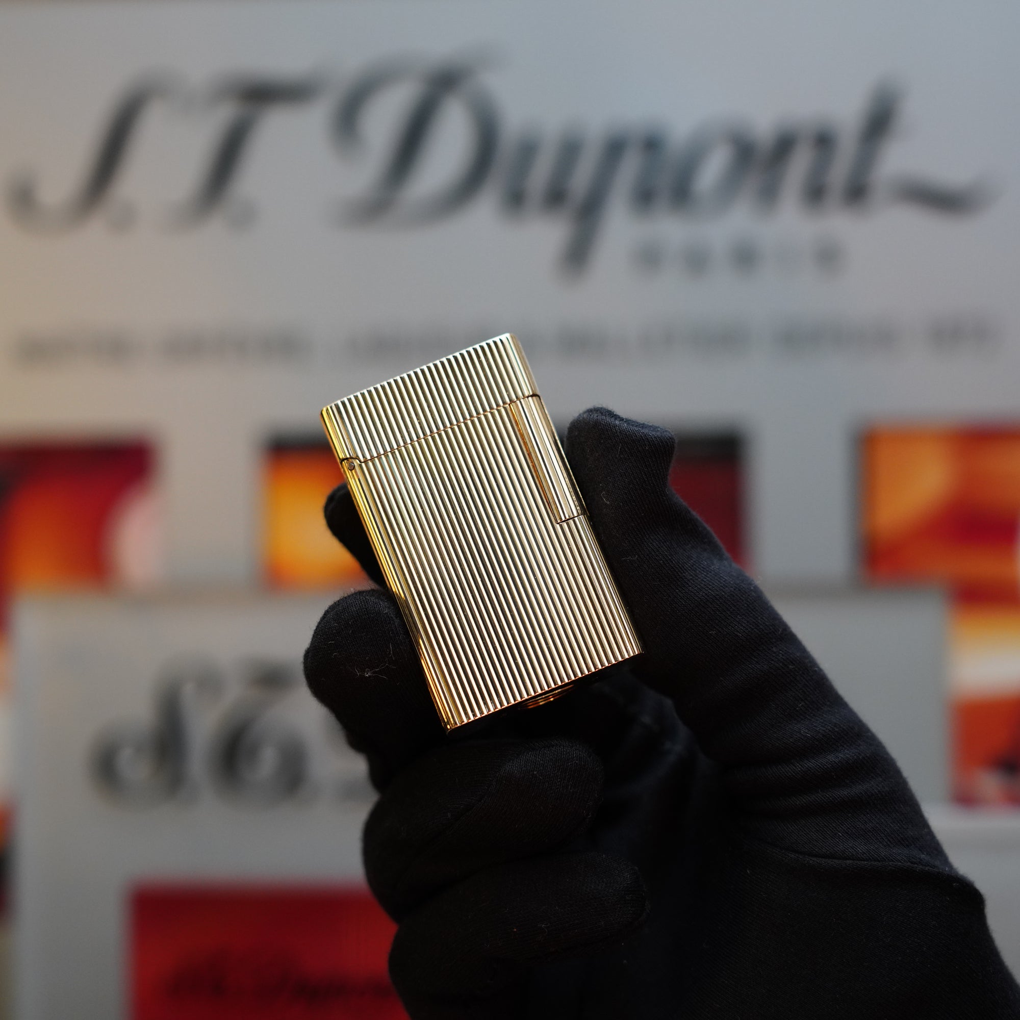 A gloved hand holds an intricate, gold lighter with a striped pattern, proudly featuring the "S.T. Dupont" branding in the background. This 1960 St Dupont BS 18k Solid Gold Lighter with 750 hallmark is a true collector's item from the 60s.