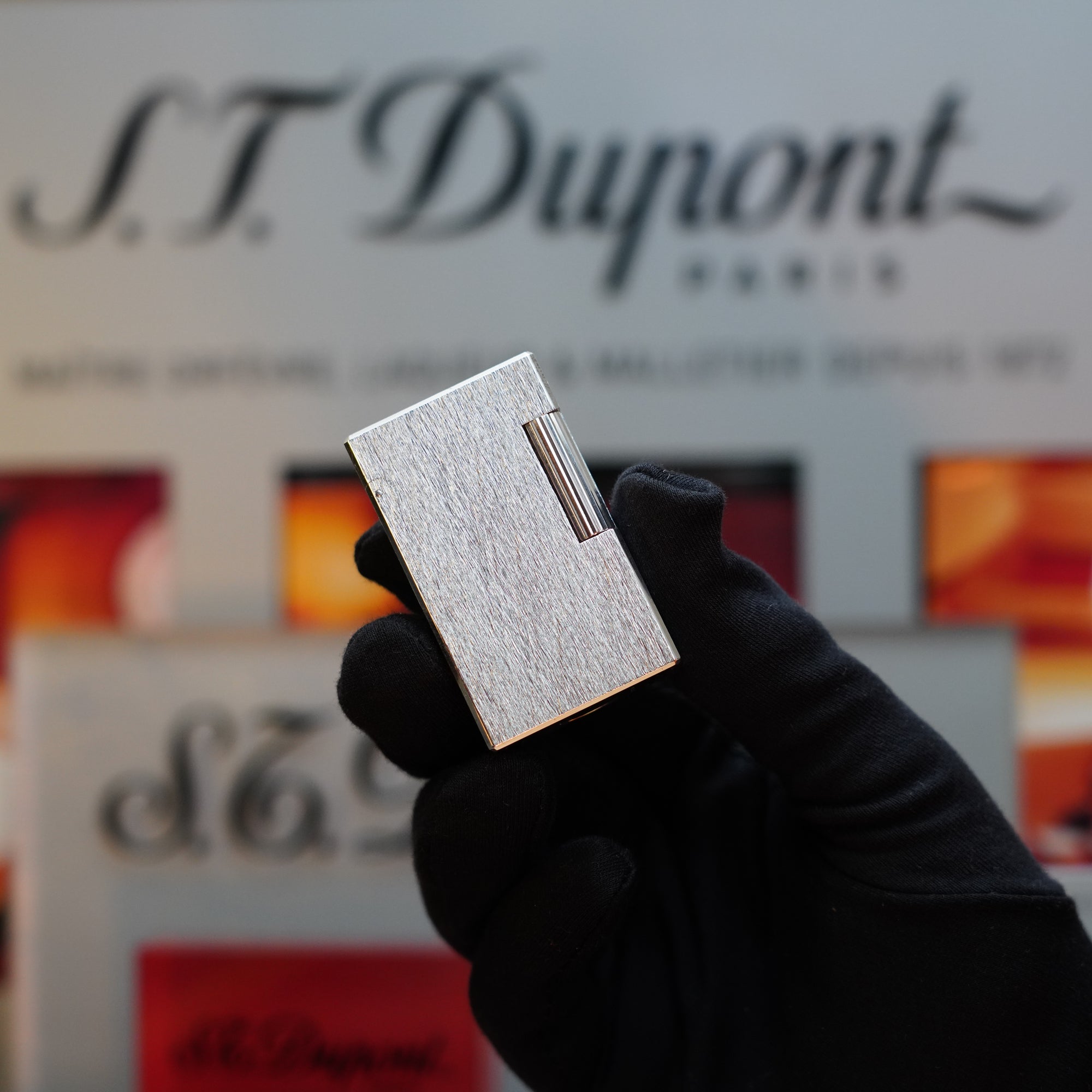 A gloved hand holds the 1980 St Dupont Heavy Silver Finish Ligne 1 Large Rare Pattern lighter in front of a blurred S.T. Dupont Paris background, highlighting this vintage S.T. Dupont masterpiece as a quintessential collector's item.