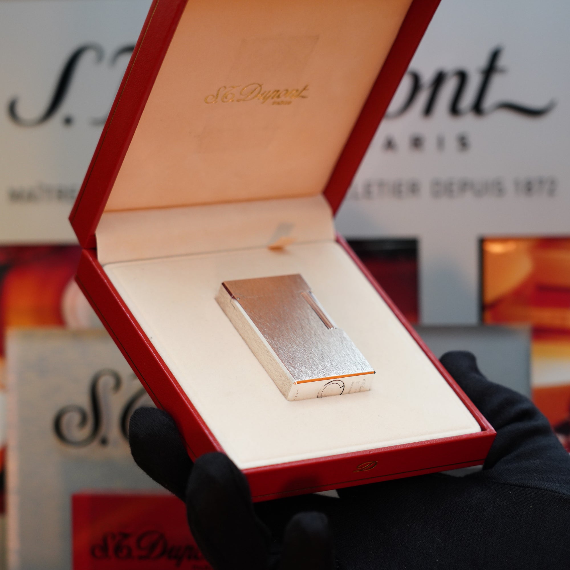 A person holding an open red box displays a 1980 St Dupont Heavy Silver Finish Ligne 1 Large Rare Pattern lighter, with "S.T. Dupont" branding visible in the background—a true collector's item.