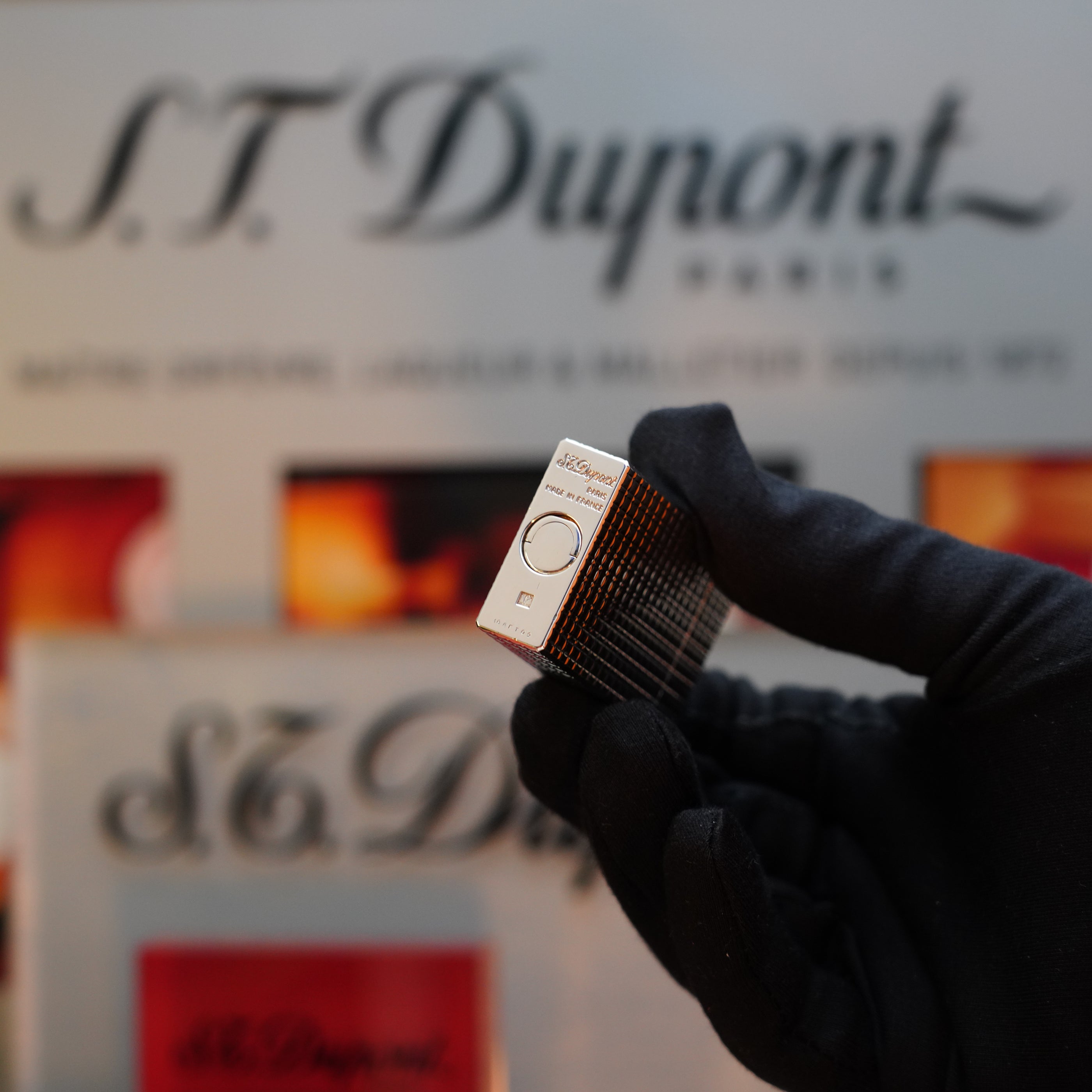 A gloved hand holds a sizable 1980 S.T. Dupont Silver Finish Rare Pattern Ligne 1 Lighter, with S.T. Dupont branding in the background.