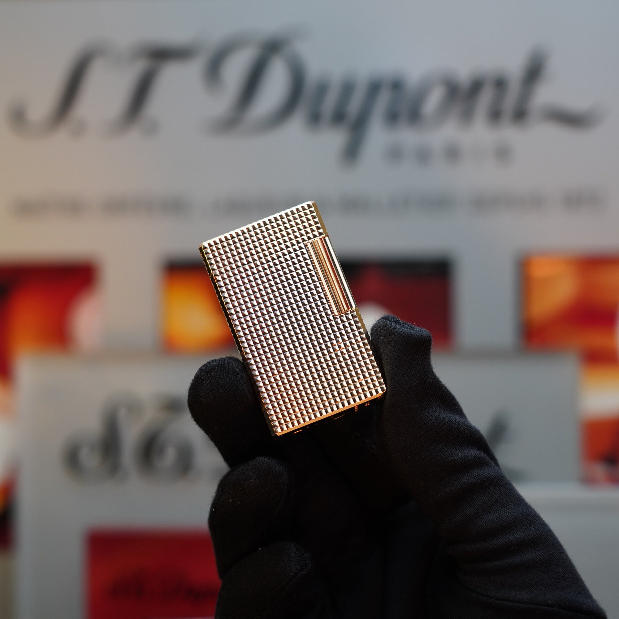 A gloved hand holds a small, silver-patterned metal object against a blurred background displaying the text "S.T. Dupont." This 1960 St Dupont BS 24k Diamond Head Gold Finish Rare Set from S.T. Dupont showcases an exquisite 24k gold finish.