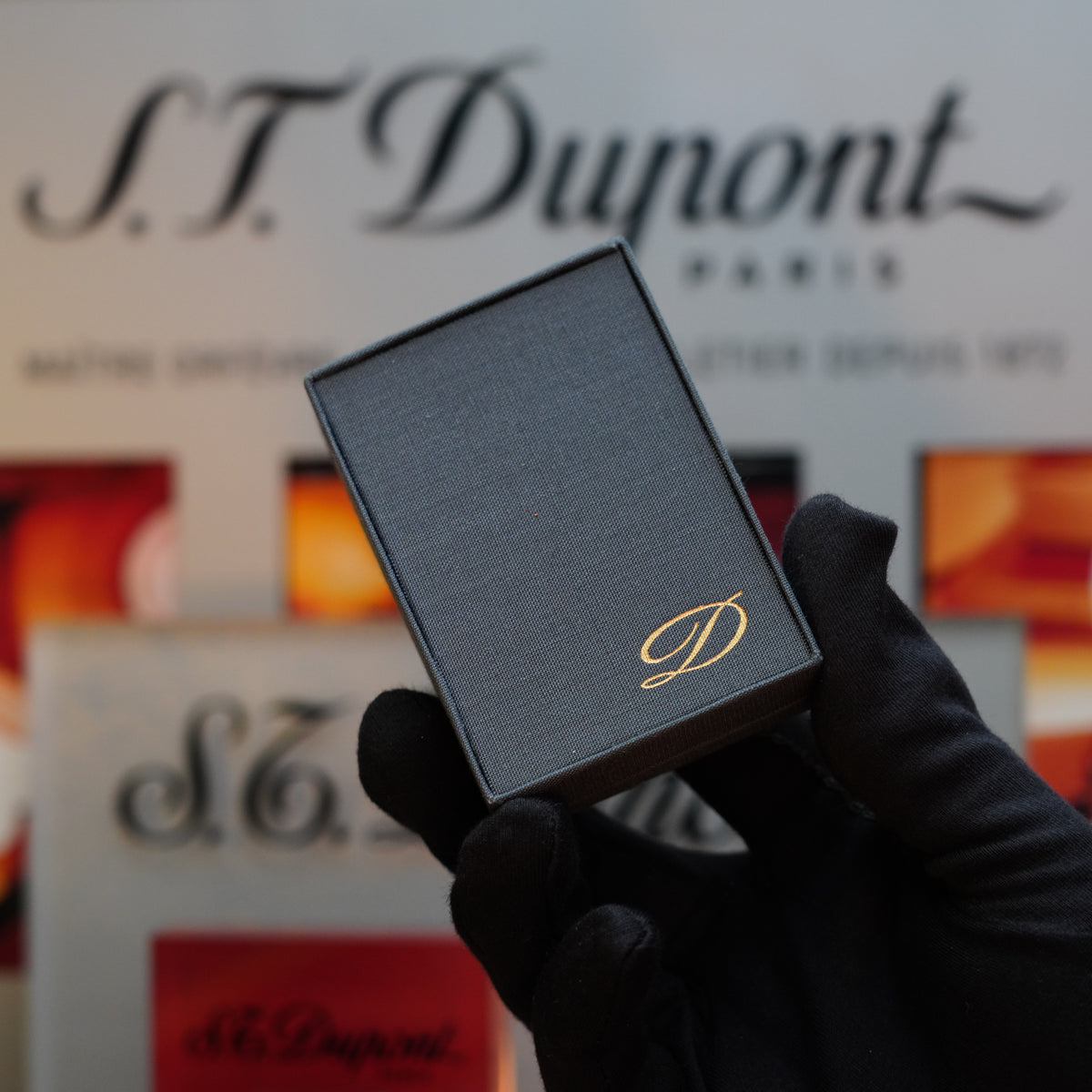 A gloved hand holds a small black box adorned with a gold 'D' emblem, hinting at the timeless elegance of the 1960 St Dupont BS 24k Diamond Head Gold Finish Rare Set. The background features the text "S.T. Dupont Paris.