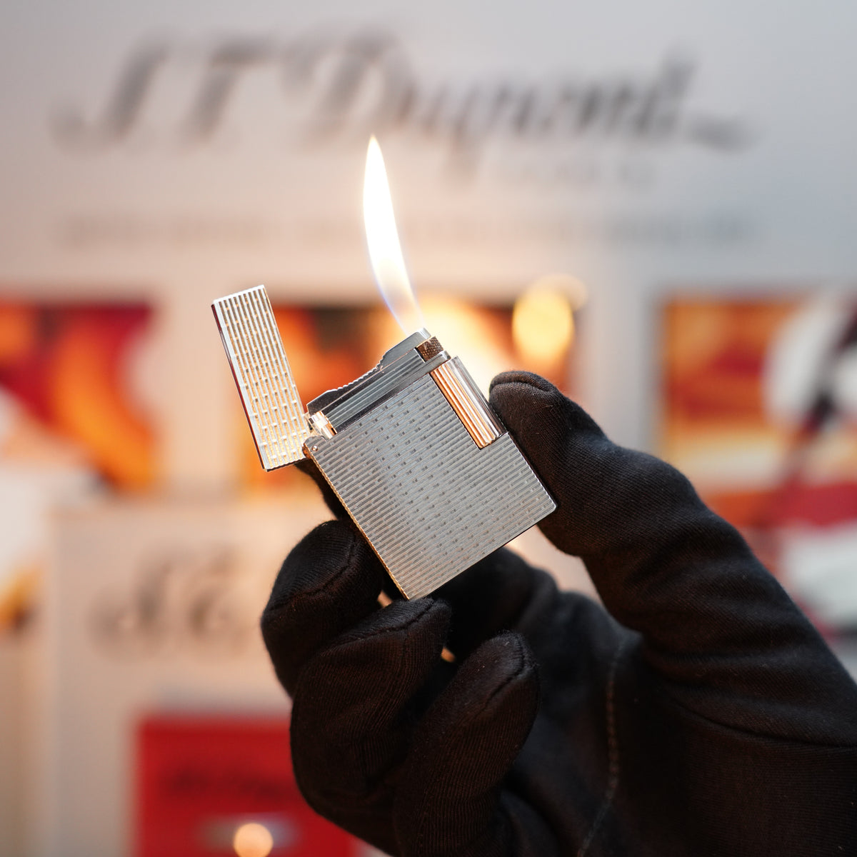 A gloved hand holds a lit S.T. Dupont Vintage 1990 lighter with a heavy silver finish and rare visual pattern, set against a blurred background.