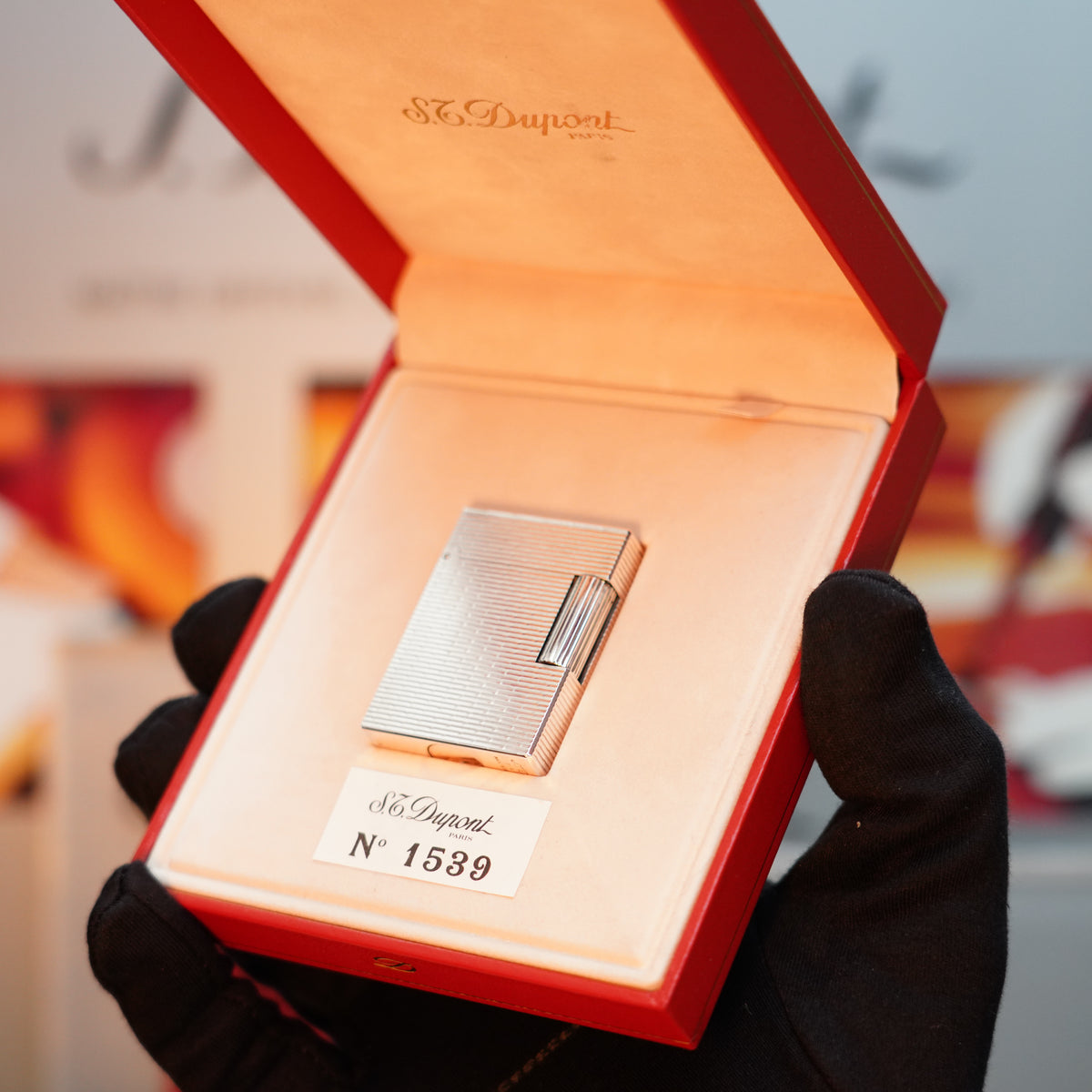 A gloved hand holds a red box showcasing a silver lighter from S.T. Dupont's Ligne 1 Series, labeled with the number 1539—a vintage, rare collector's piece known as the Vintage 1990 S.T. Dupont Heavy Silver Finish Rare Visual Pattern Ligne 1 Lighter.