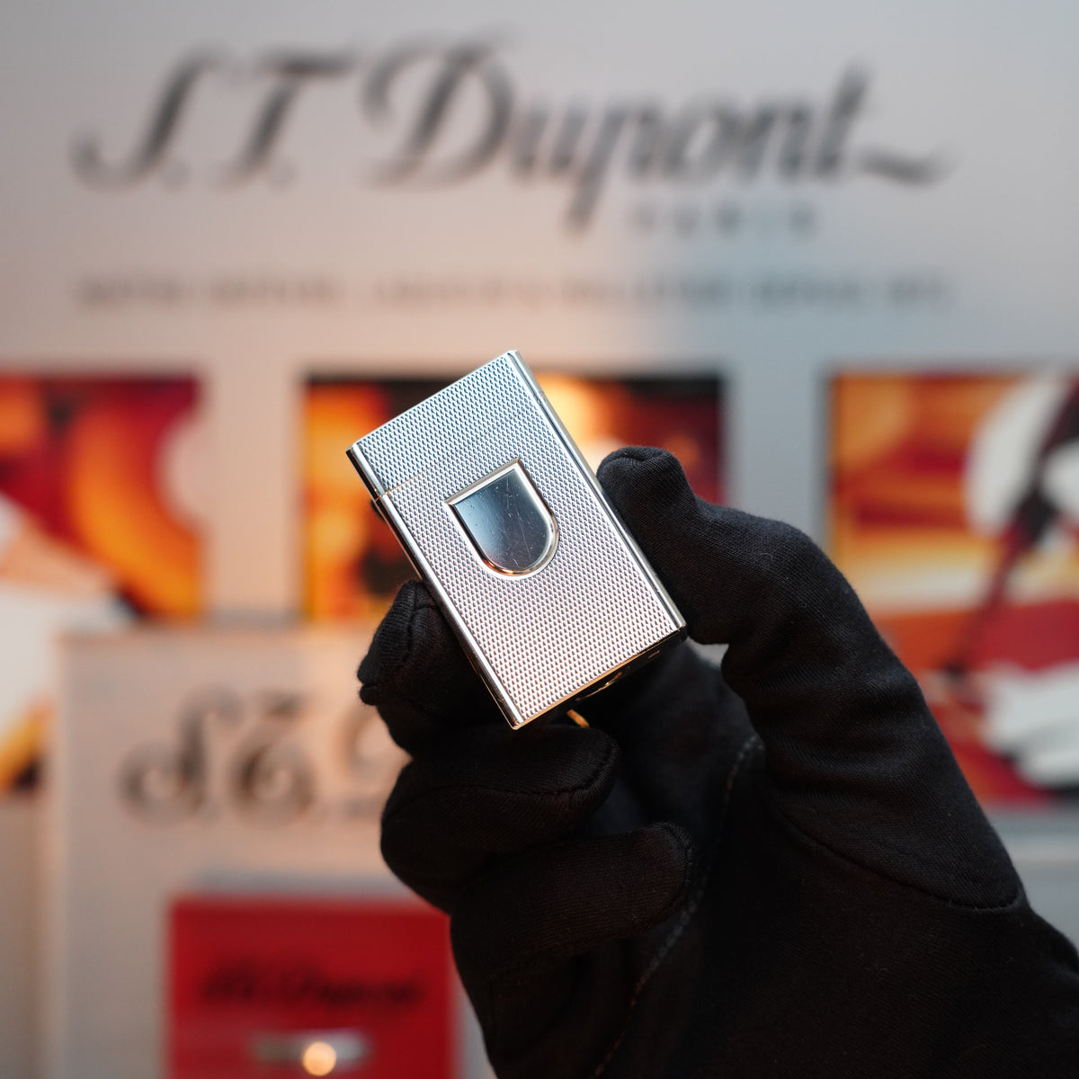 A gloved hand holds a Vintage 1980 St Dupont Ligne 1 lighter, featuring a heavy silver finish with a fine hobnail pattern, against a blurred background showcasing the S.T. Dupont brand name.