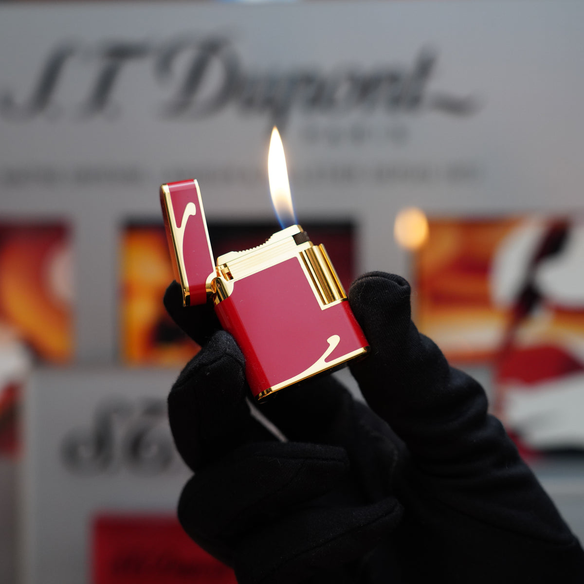 A gloved hand holds a Vintage 1990 St Dupont rare Ornee Soubreny 24k Gold Finish Red Passion Lacquer Lighter, its flame dancing elegantly as the name "S.T. Dupont" gleams in the background.