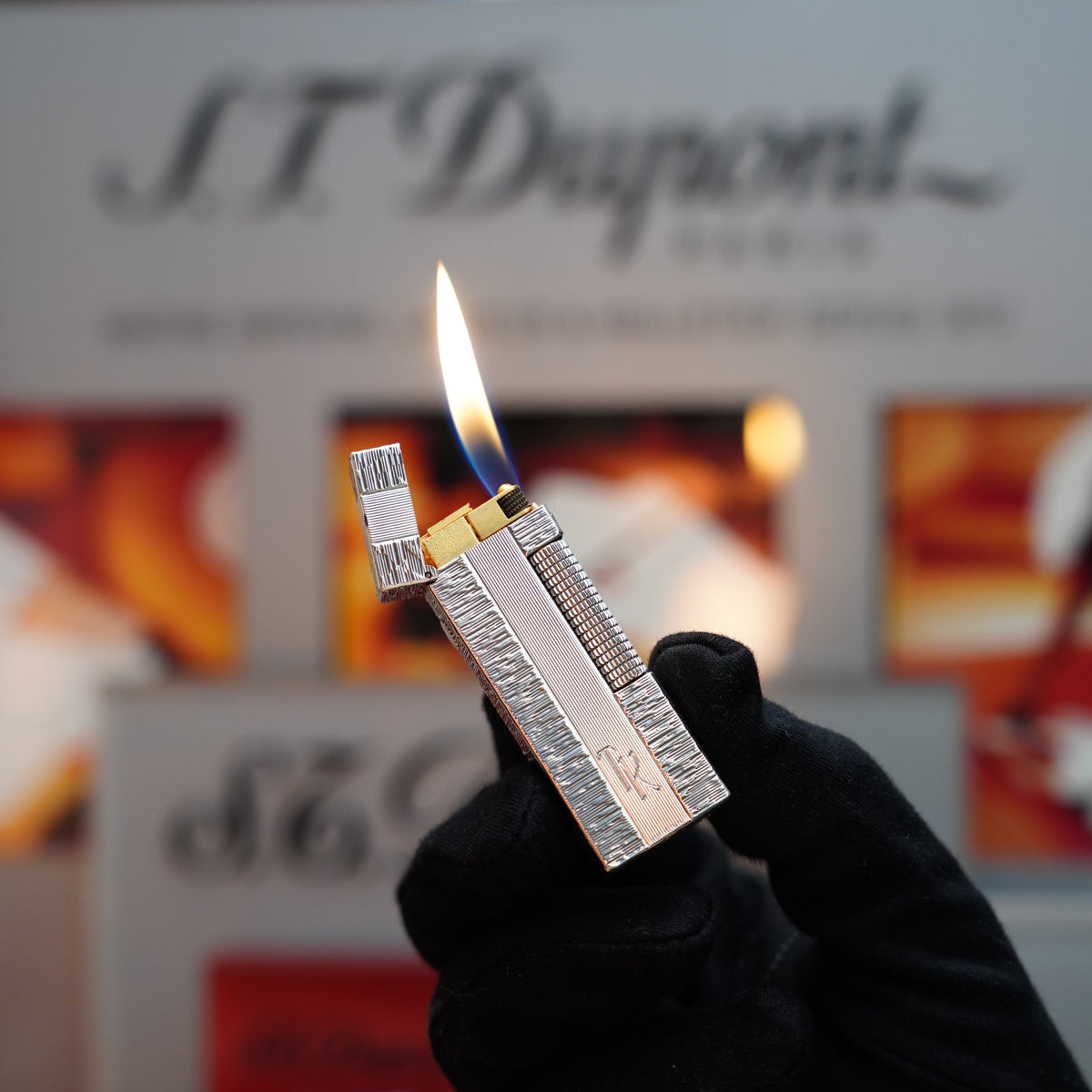 A gloved hand holds an exquisite S.T. Dupont lighter, its flame flickering brilliantly against a blurred backdrop, reminiscent of the elegance found in a Vintage Dunhill Rollagas Limited Edition Solid Silver 925 Lines with Hallmark Lighter.