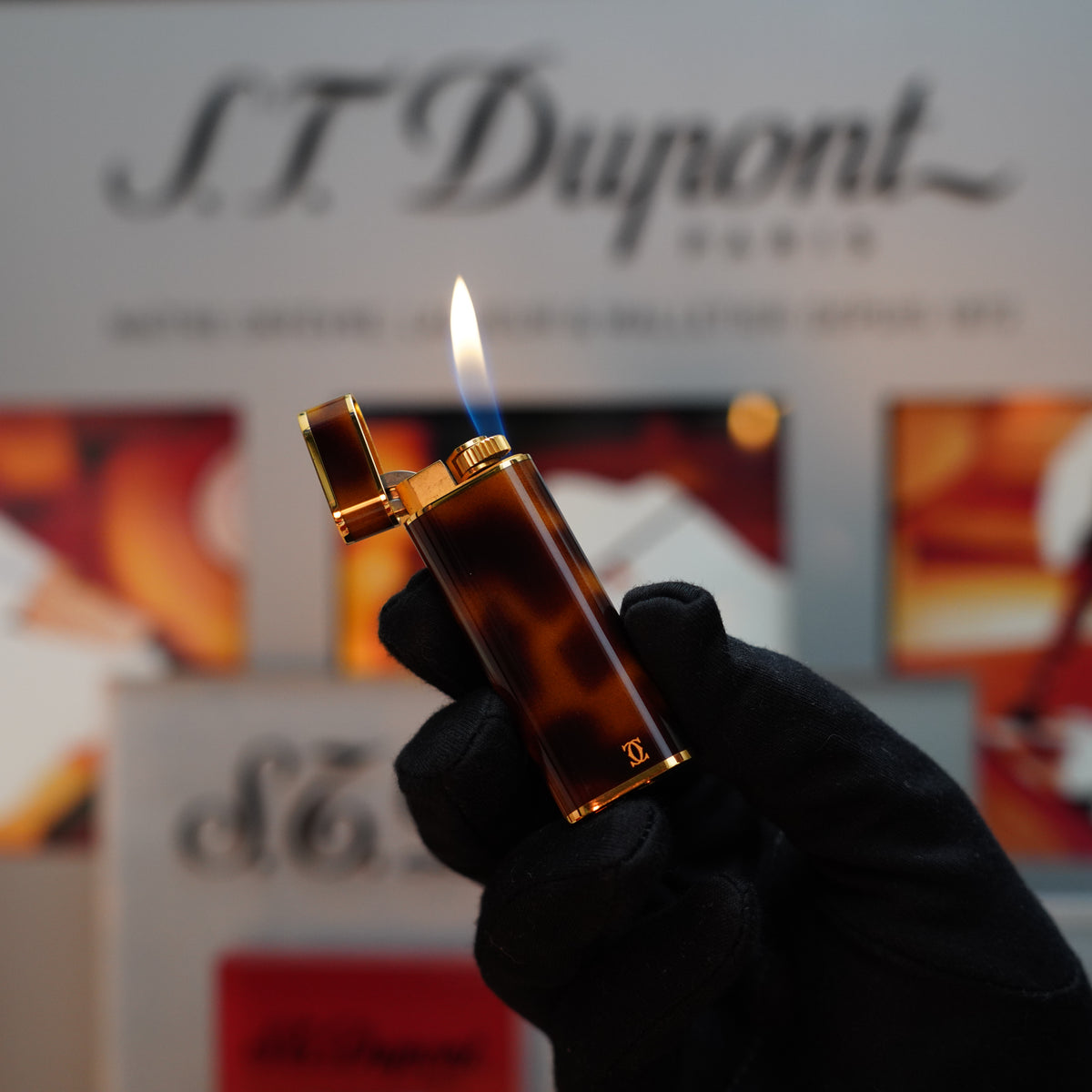 A gloved hand holds a Vintage 1980 Cartier Le Must Lighter, showcasing its elegant tortoiseshell lacquer oval design with the iconic Panther motif. The background subtly features blurred branding, enhancing the allure of its rare 24k gold heavy finish.